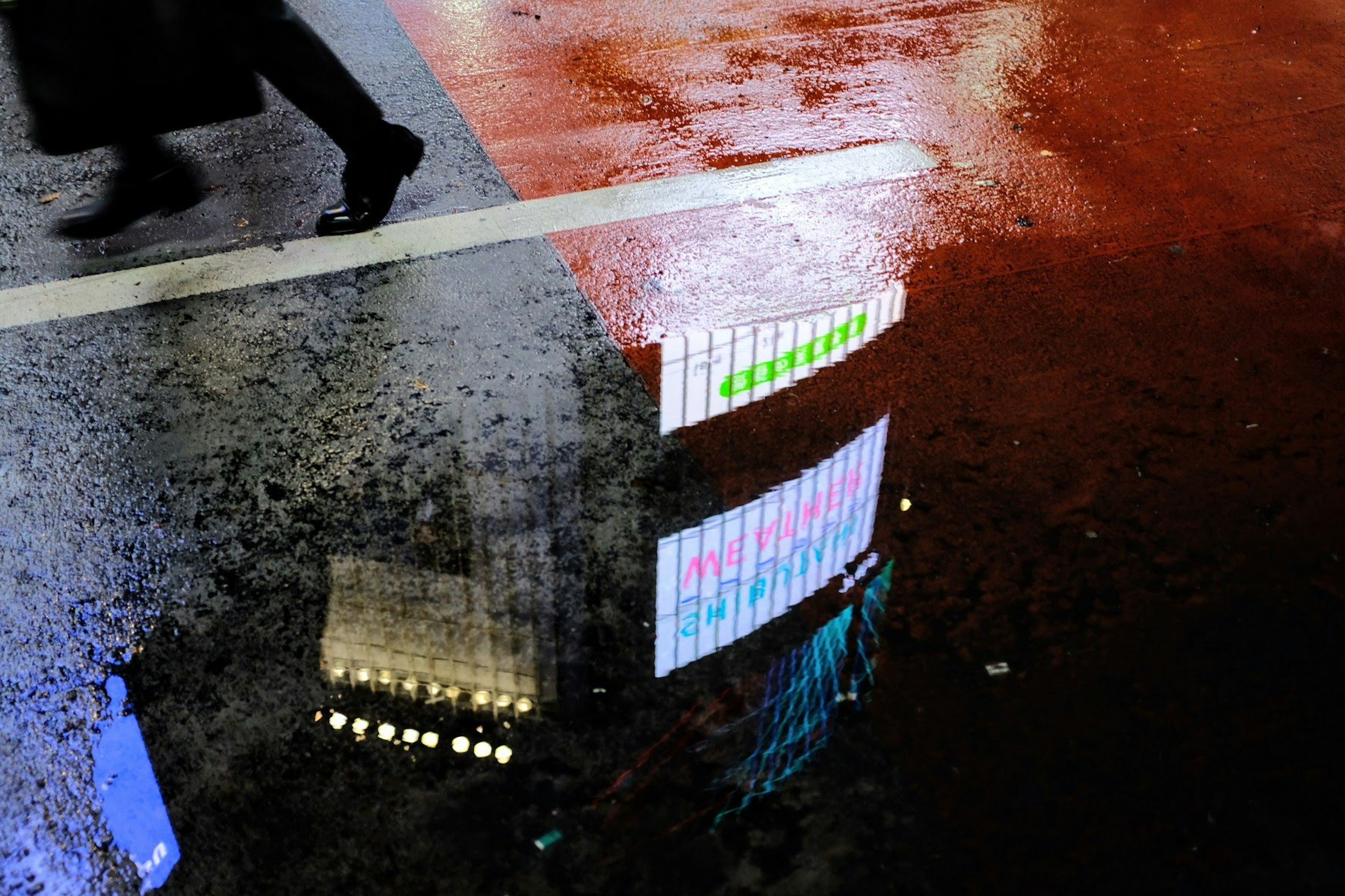 雨に濡れた歩道に映るネオンの反射と人の足元