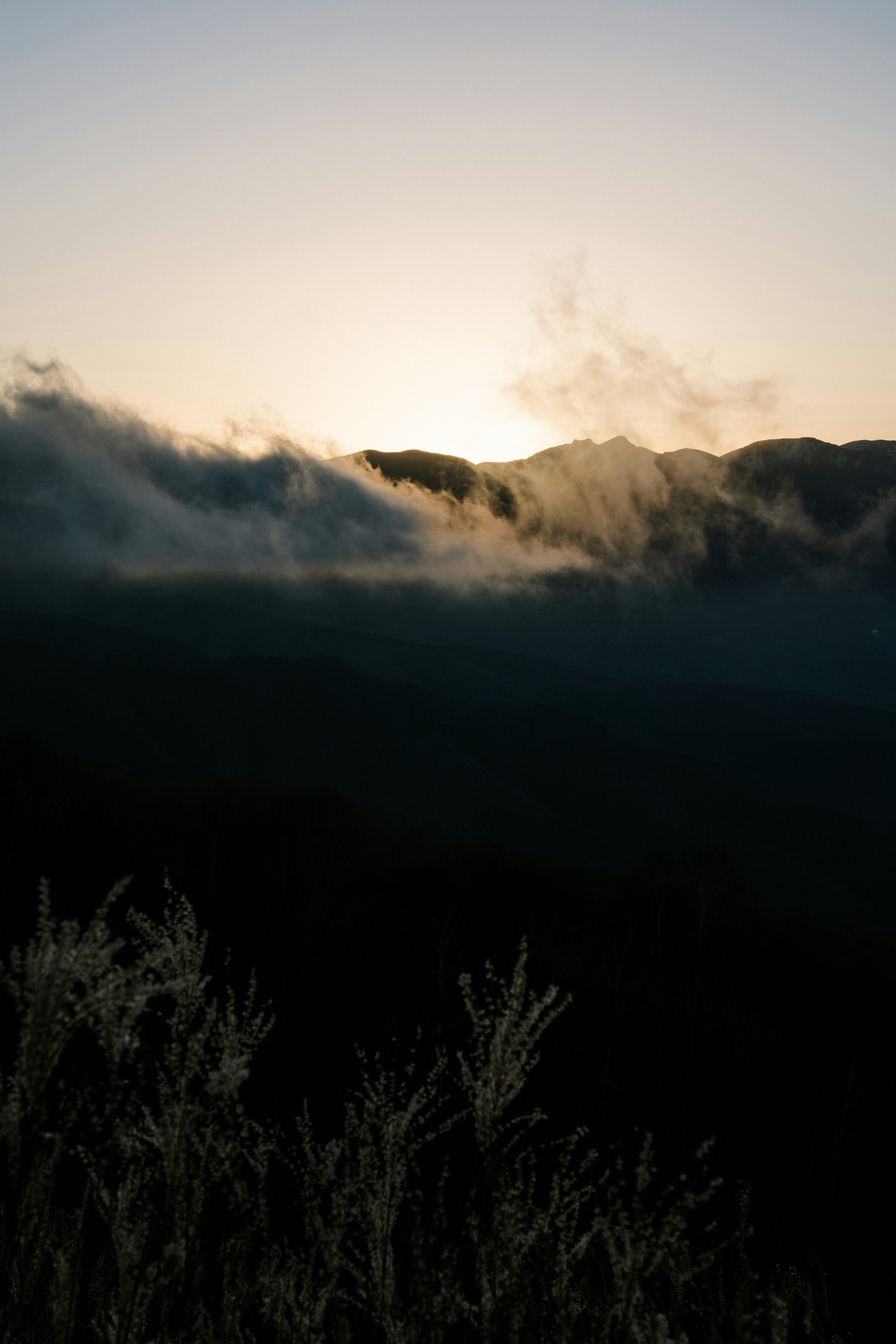 曇り空の背後に夕日が昇る山々のシルエット