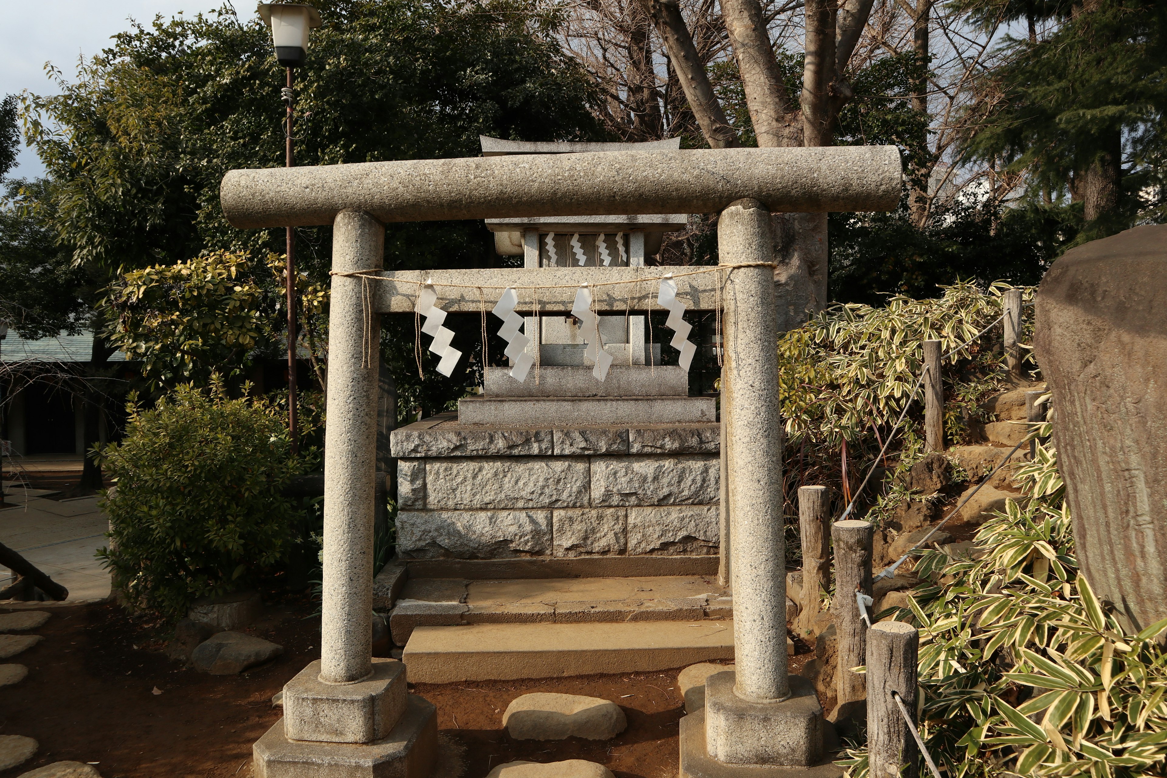 Cổng torii và bàn thờ bằng đá trong khung cảnh yên tĩnh được bao quanh bởi cây cối