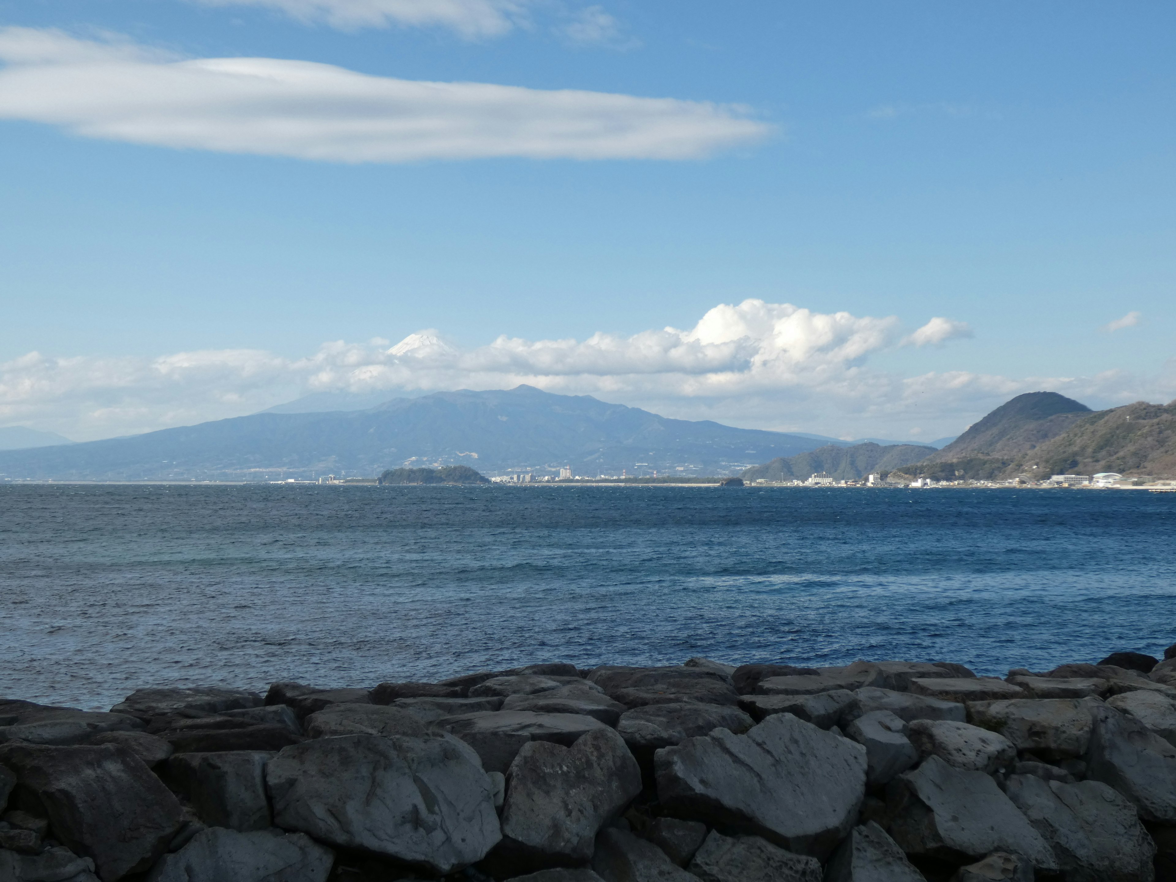 Scenic view of a blue ocean under white clouds with mountains in the background