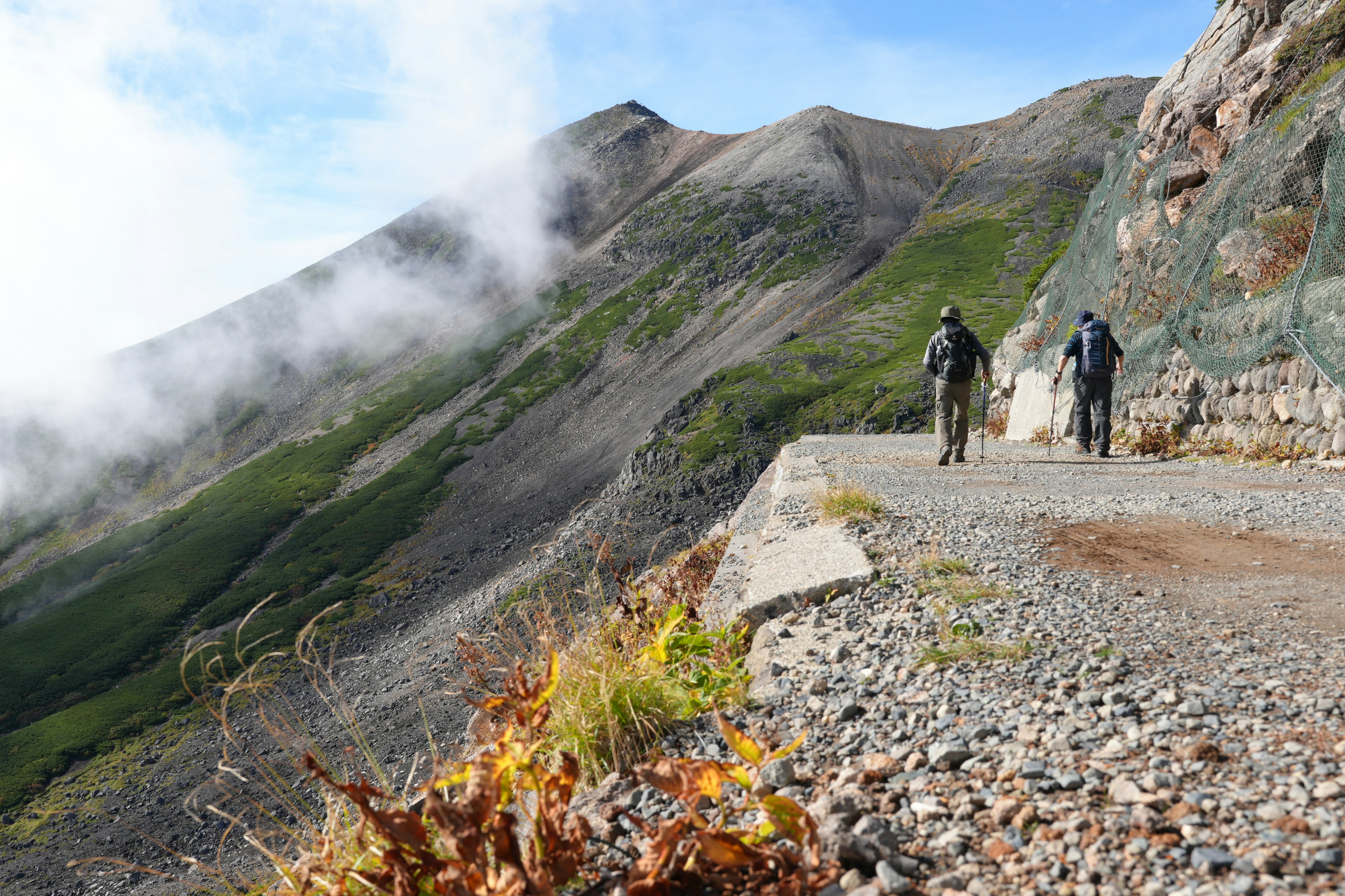 二人の登山者が山道を歩いている風景 緑の山と雲が背景にある