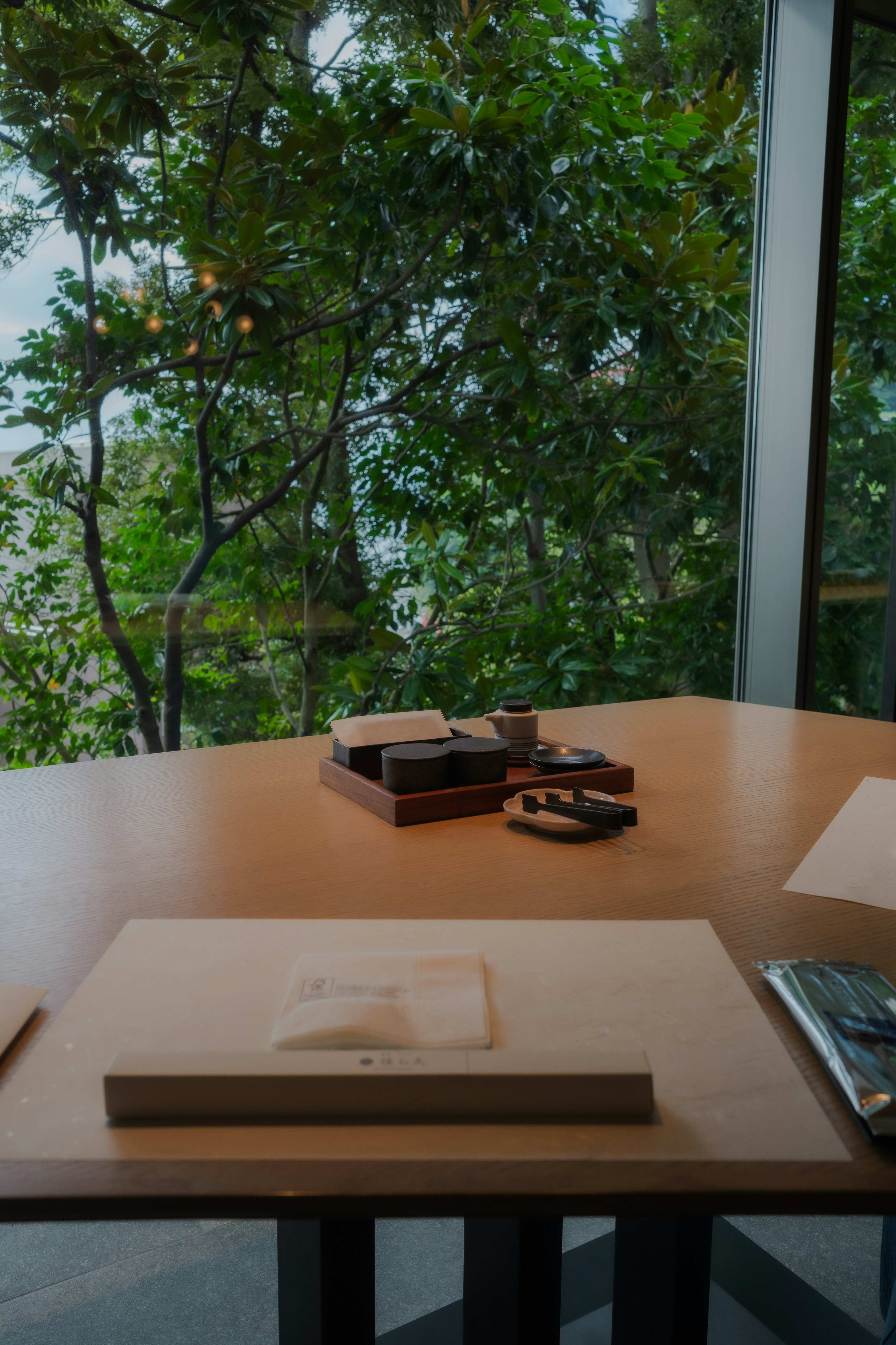 Tisch mit Schreibwaren und Büchern mit Blick auf grüne Bäume durch ein Fenster