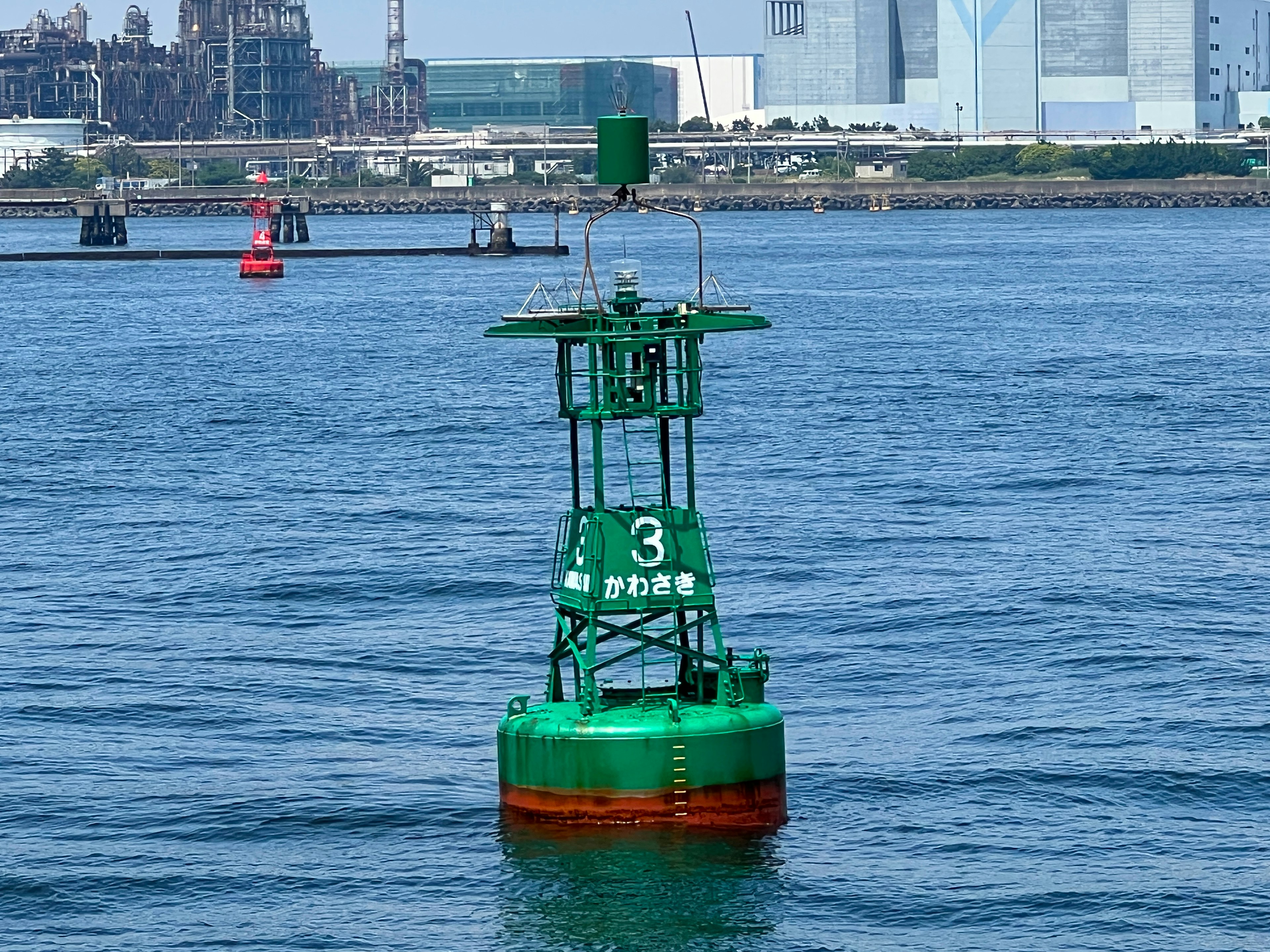 Bouée verte flottant sur l'eau avec des usines et des bâtiments en arrière-plan