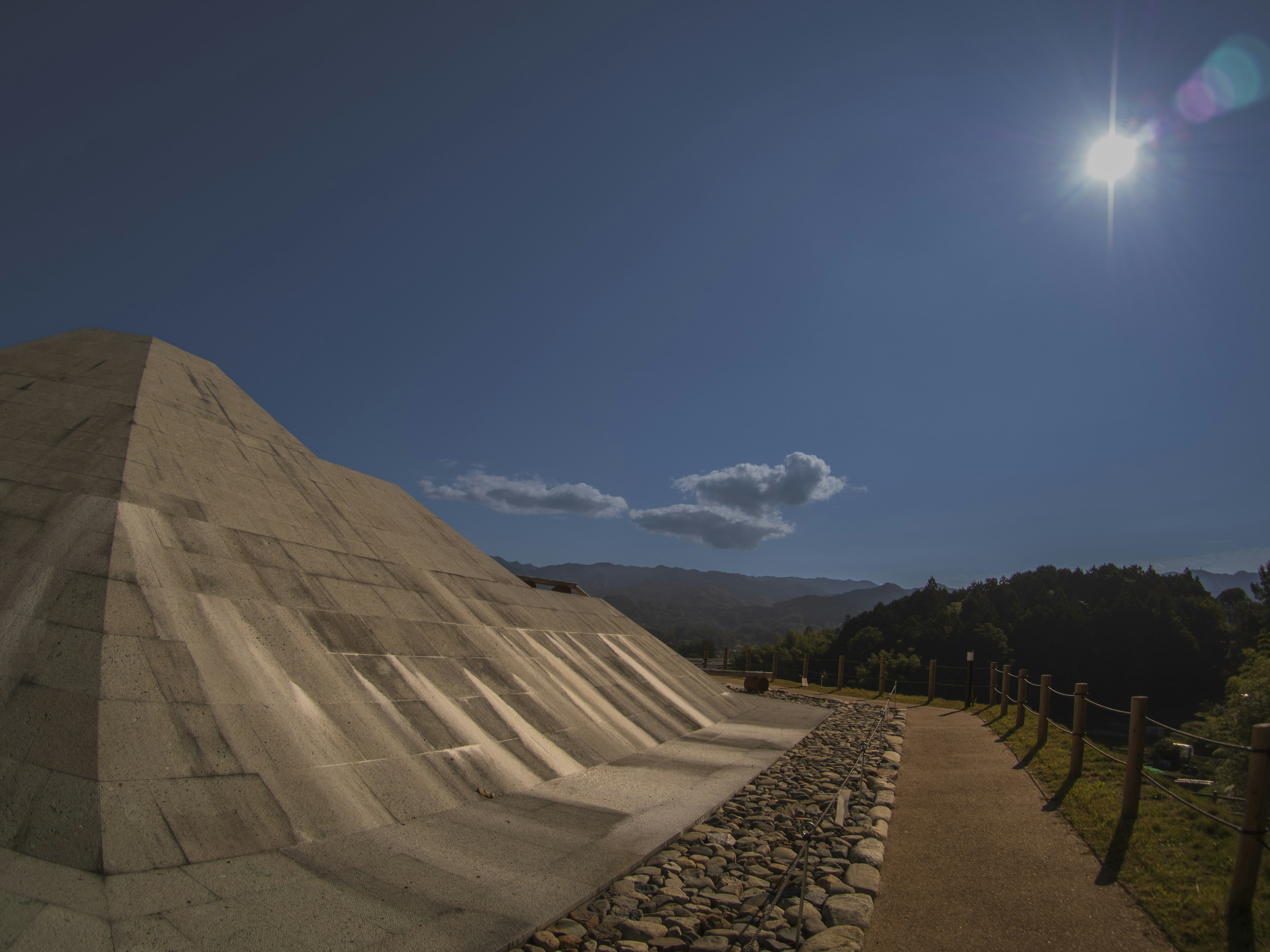 A large structure under a blue sky with a pathway beside it