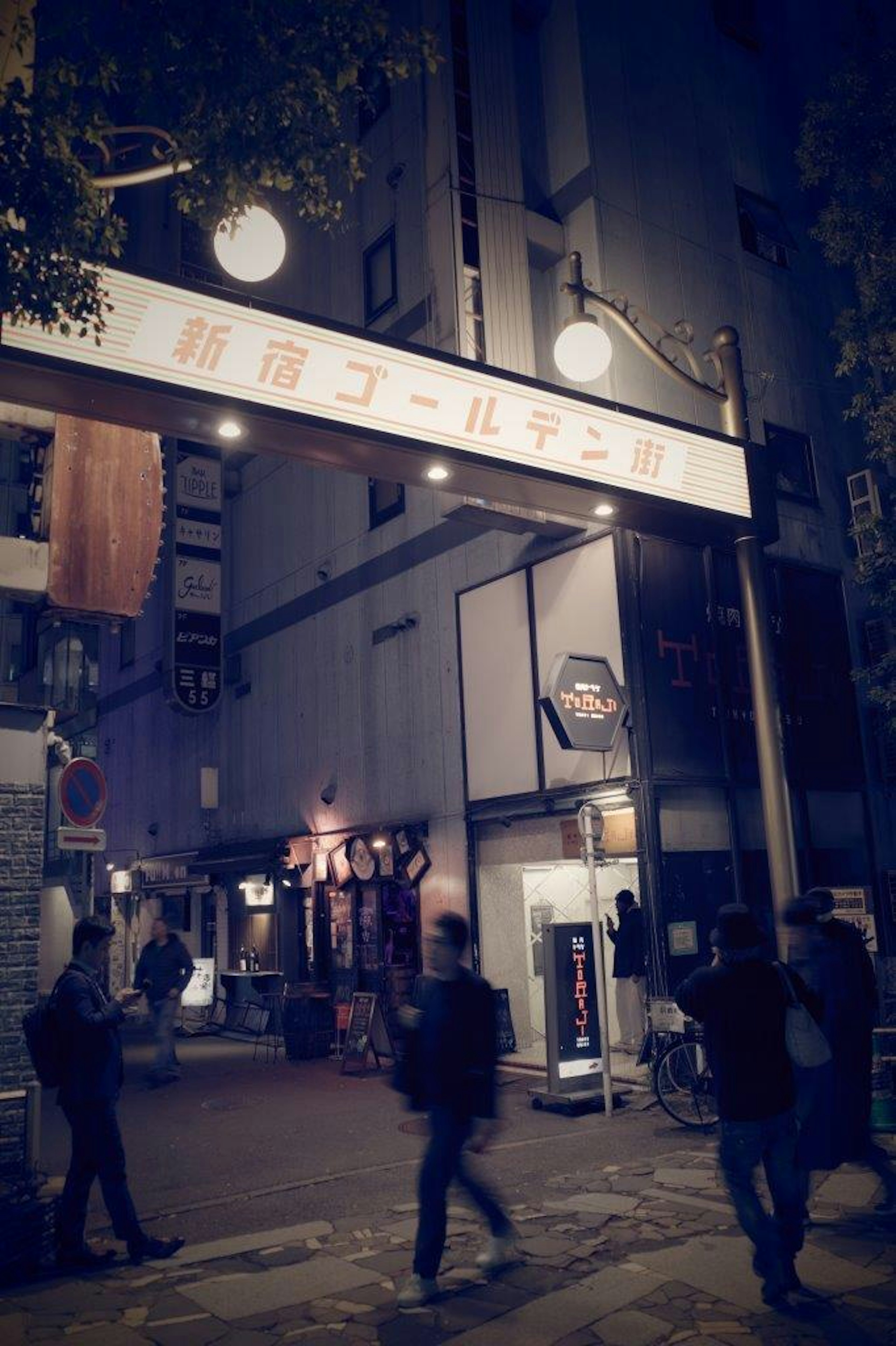 People walking under an archway sign in a nighttime urban setting