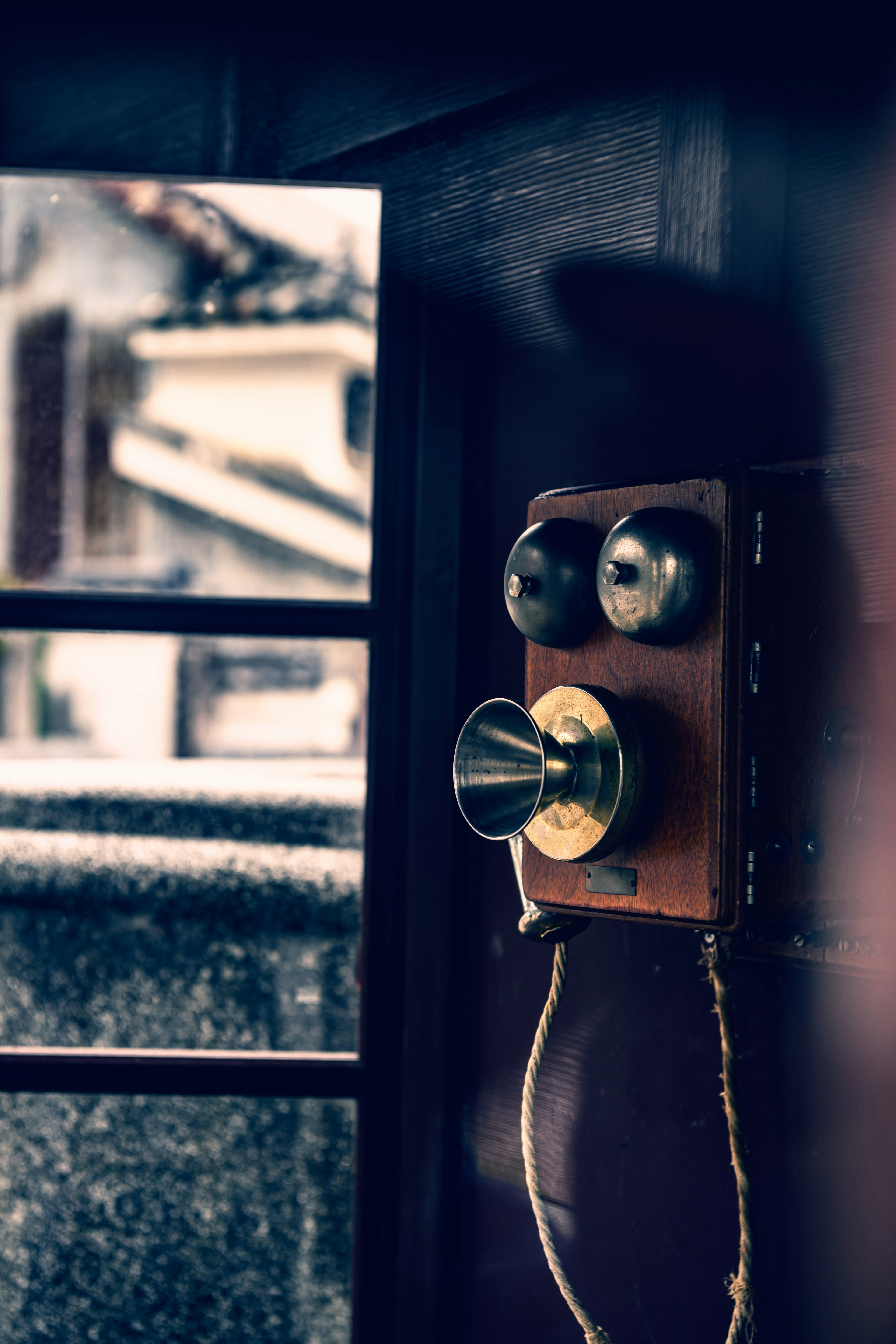 An antique telephone mounted on a wall near a window