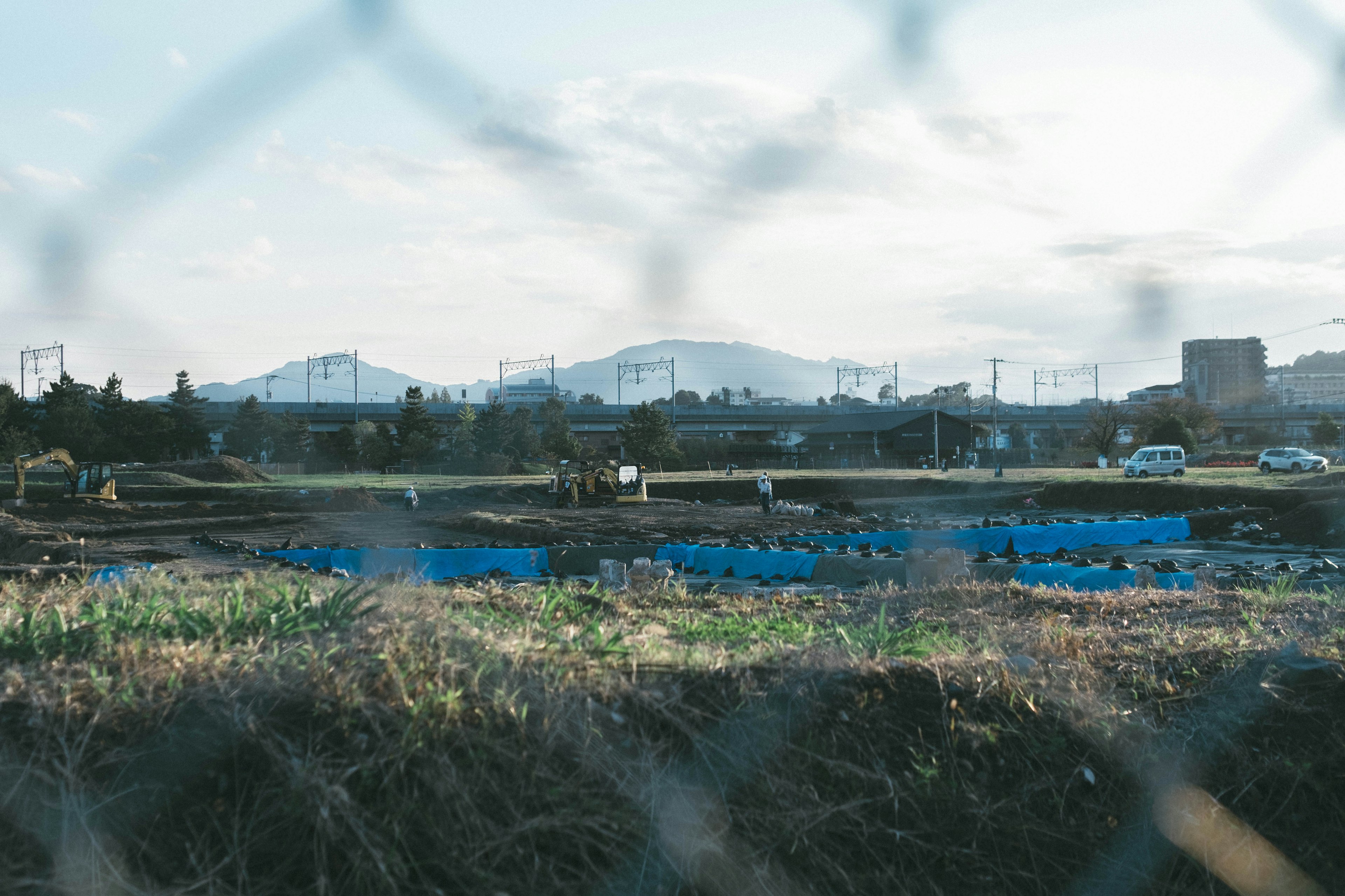 Blick auf landwirtschaftliche Flächen und entfernte Berge durch einen Zaun