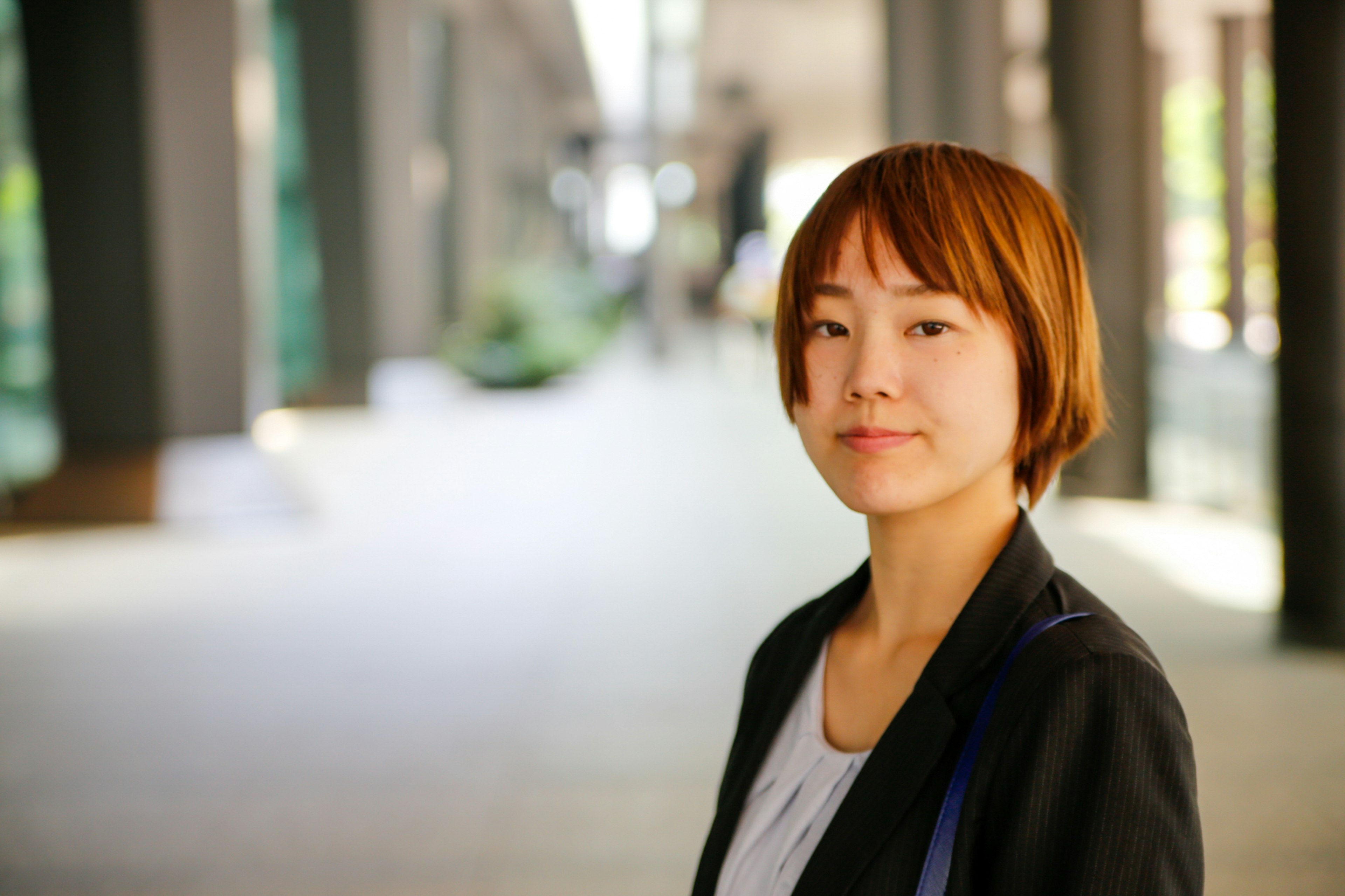 A woman with short hair standing against a blurred urban backdrop