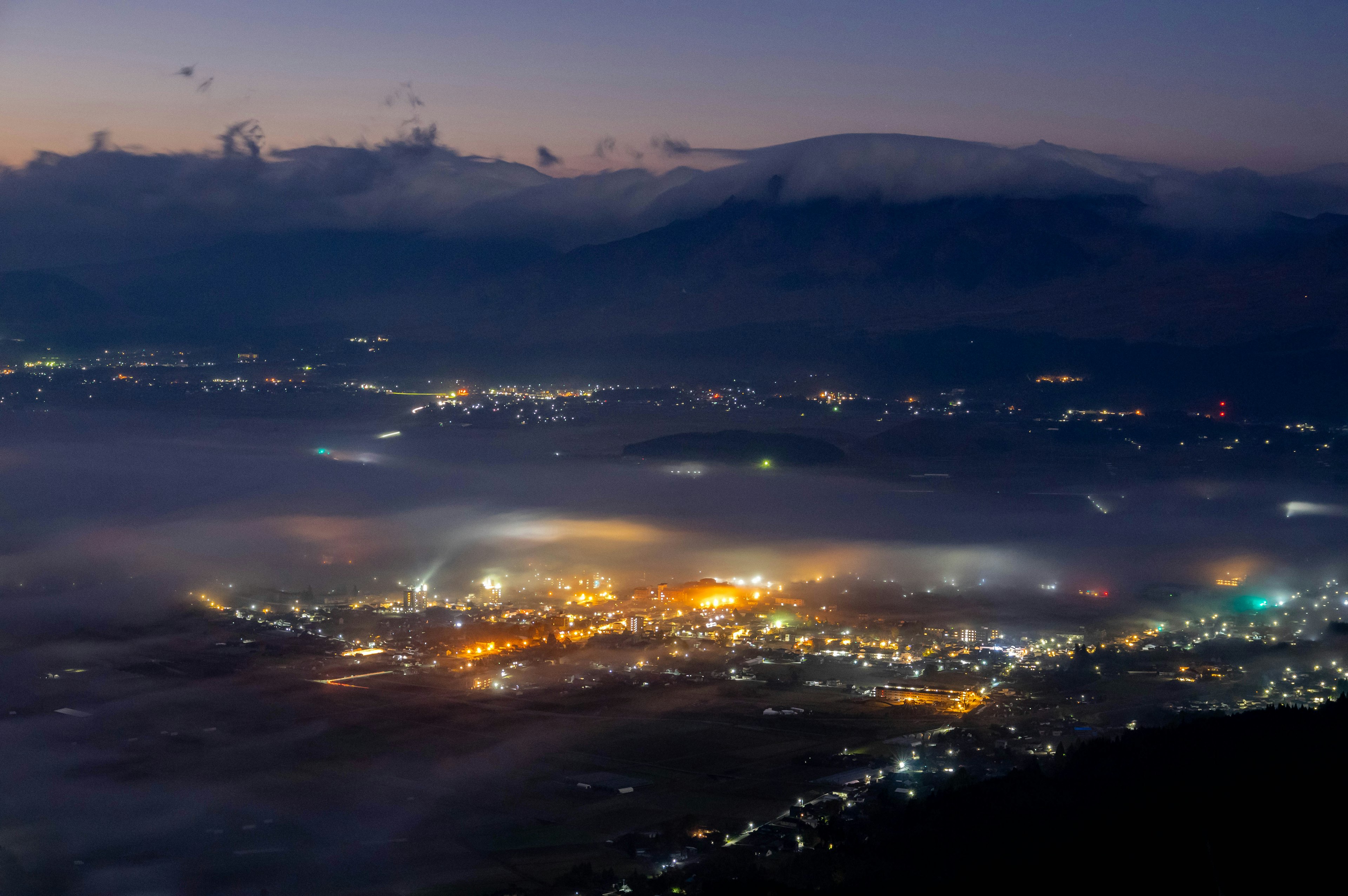 Vue d'une montagne la nuit montrant les lumières d'une ville enveloppée de brouillard