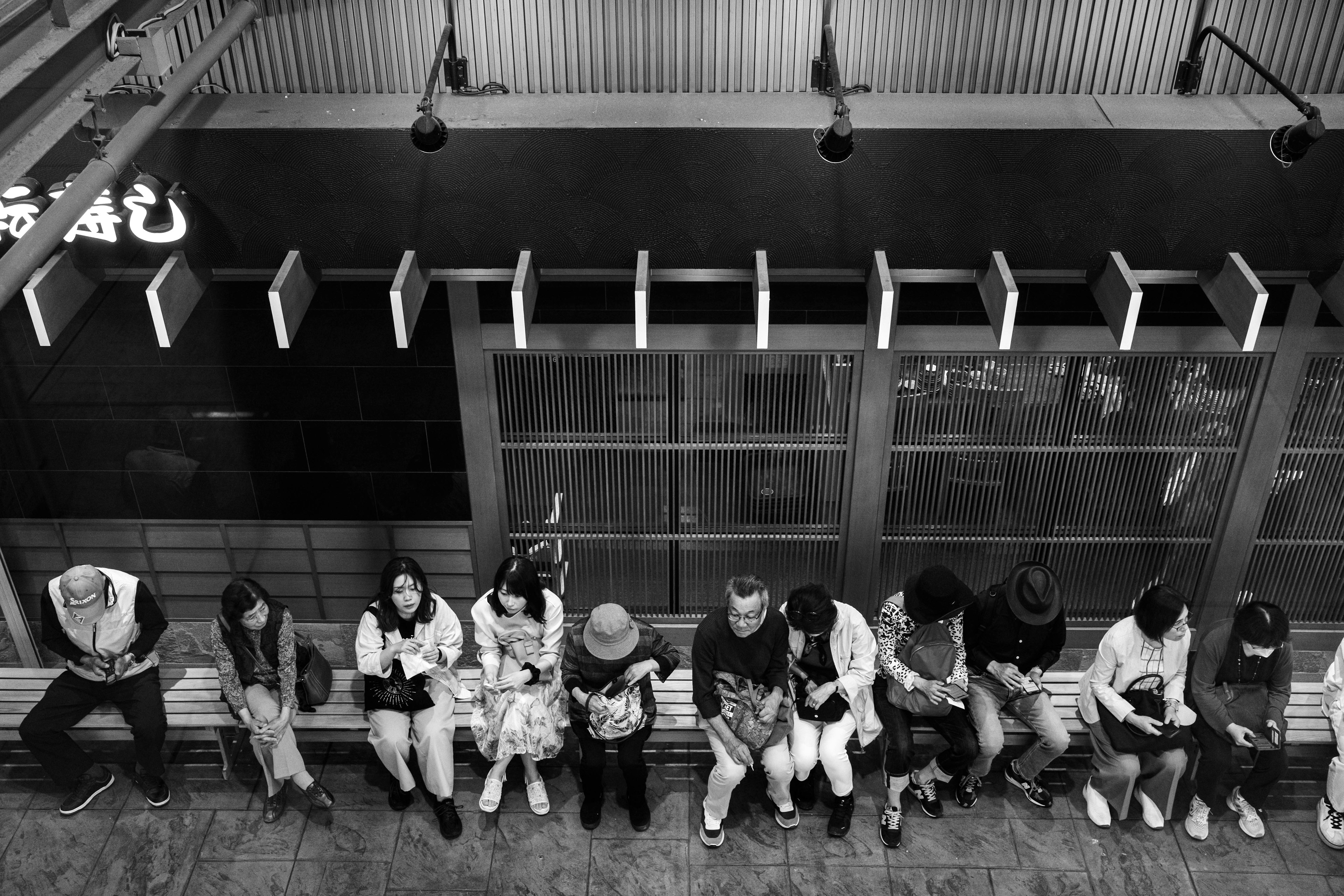 Black and white image of people sitting in a row on a bench