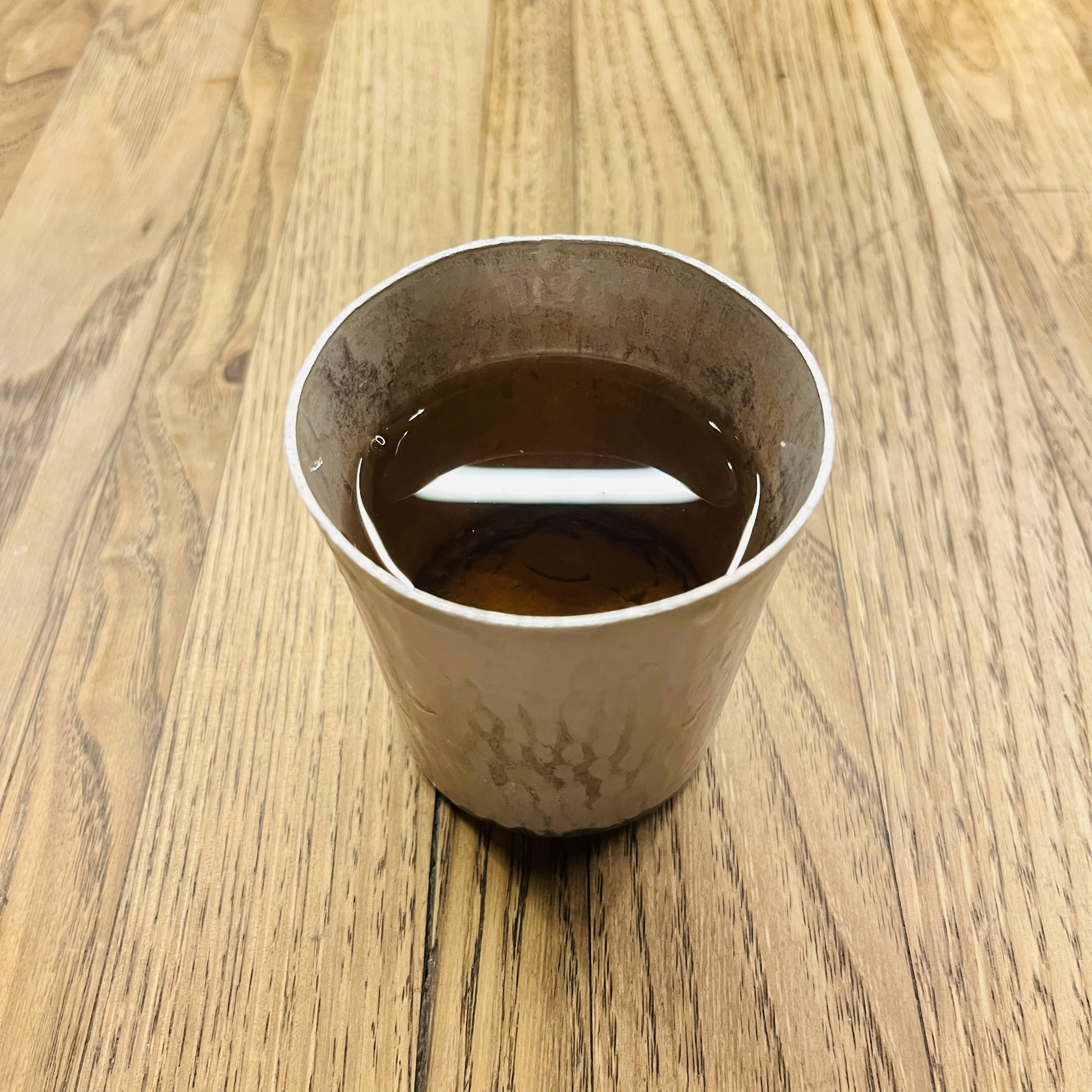 木のテーブルの上に置かれた茶色の液体の入った白いカップ