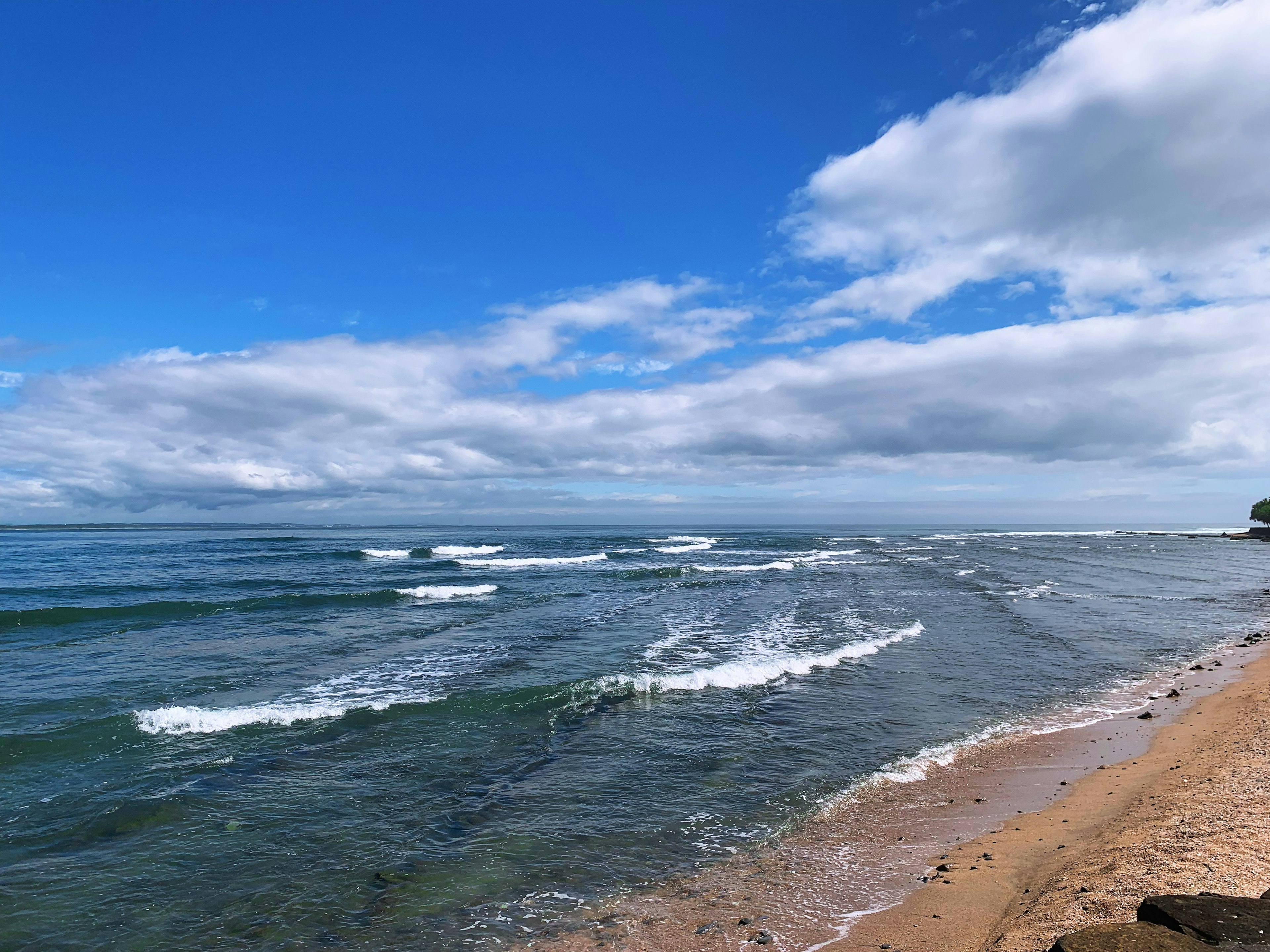 Scène côtière avec des vagues s'écrasant sur le rivage sous un ciel bleu et des nuages blancs