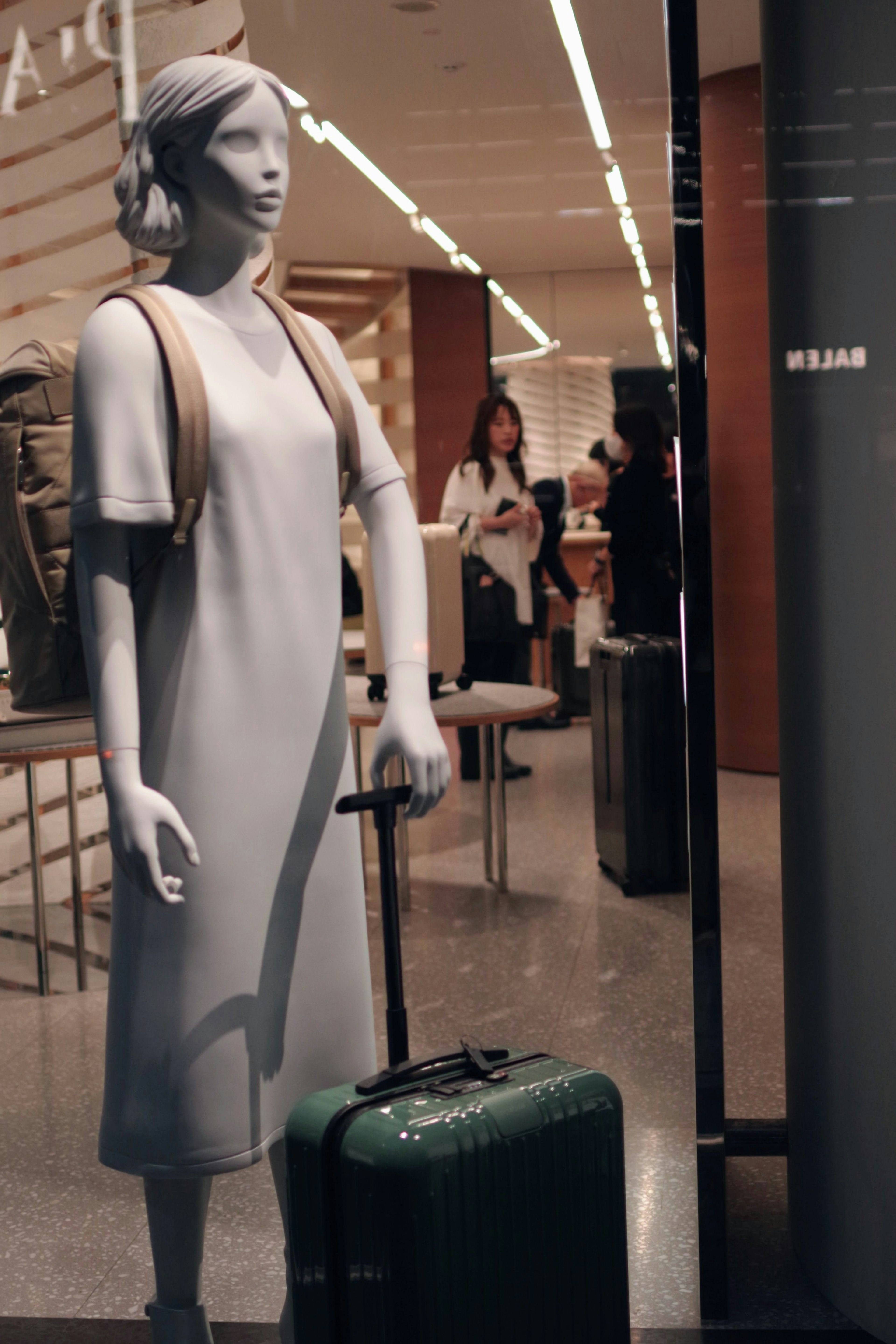 Maniquí en escaparate sosteniendo una maleta verde con atuendo casual