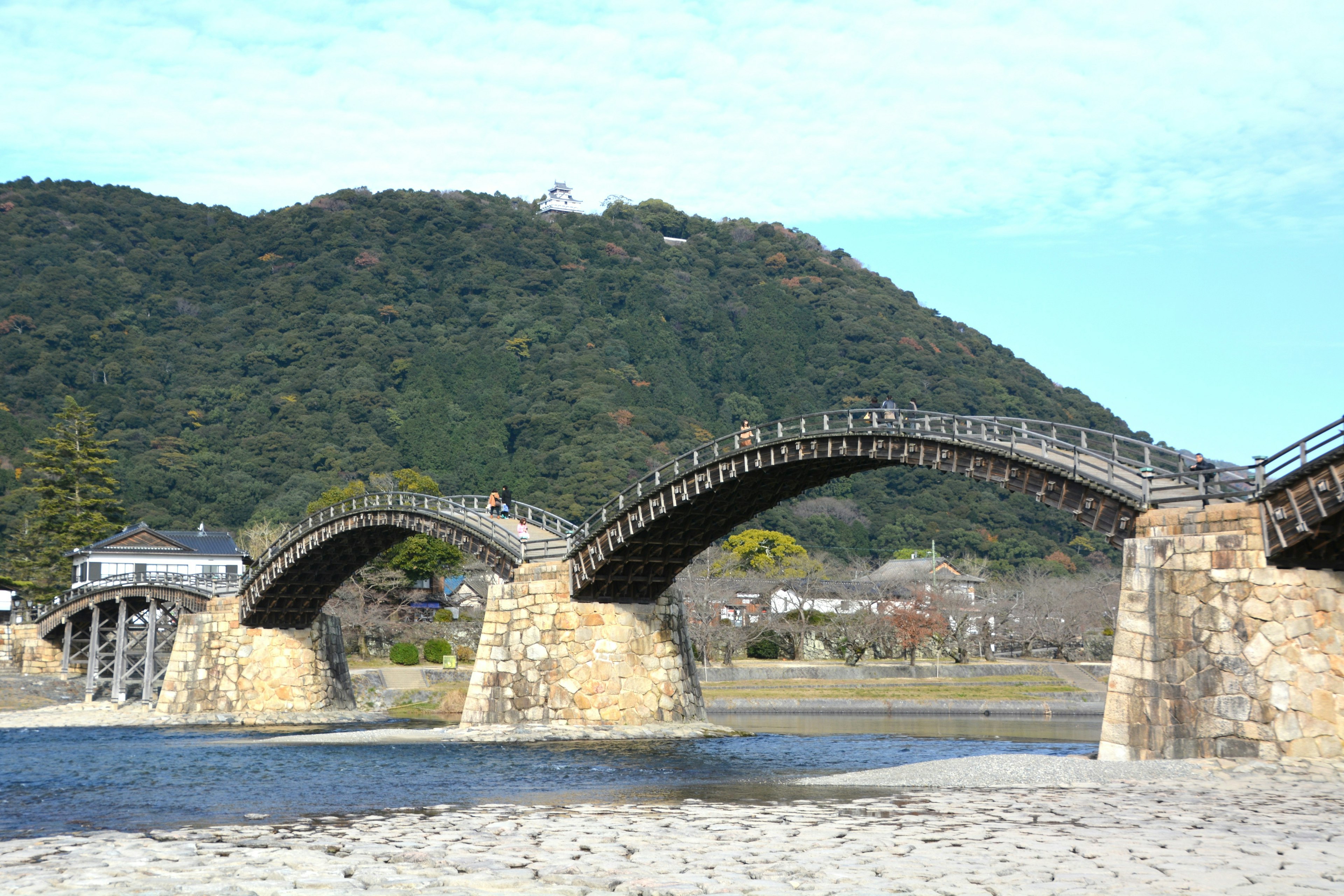 A scenic wooden arch bridge spanning a flowing river with hills in the background