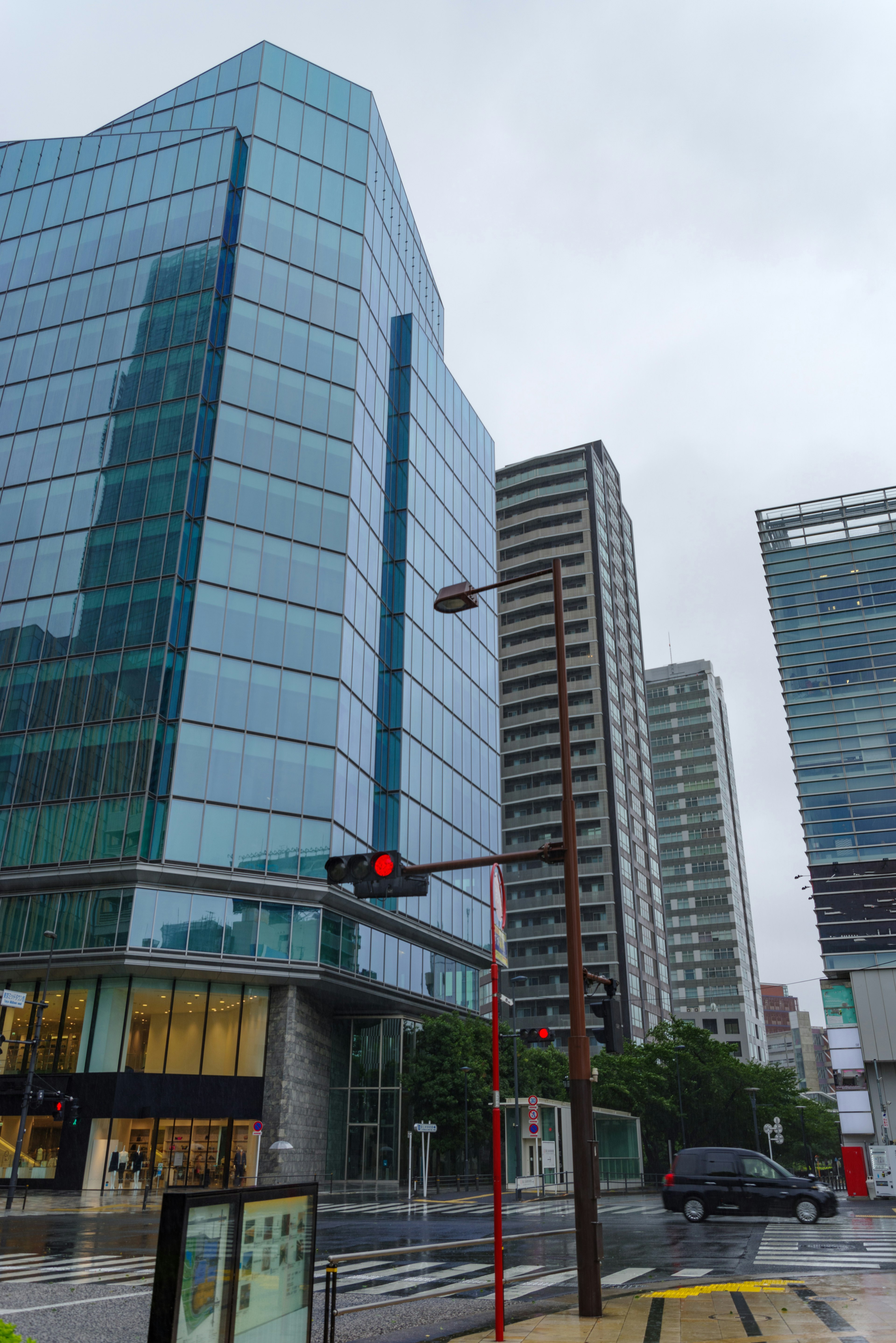 Cityscape with tall buildings featuring a prominent blue glass structure in rainy weather