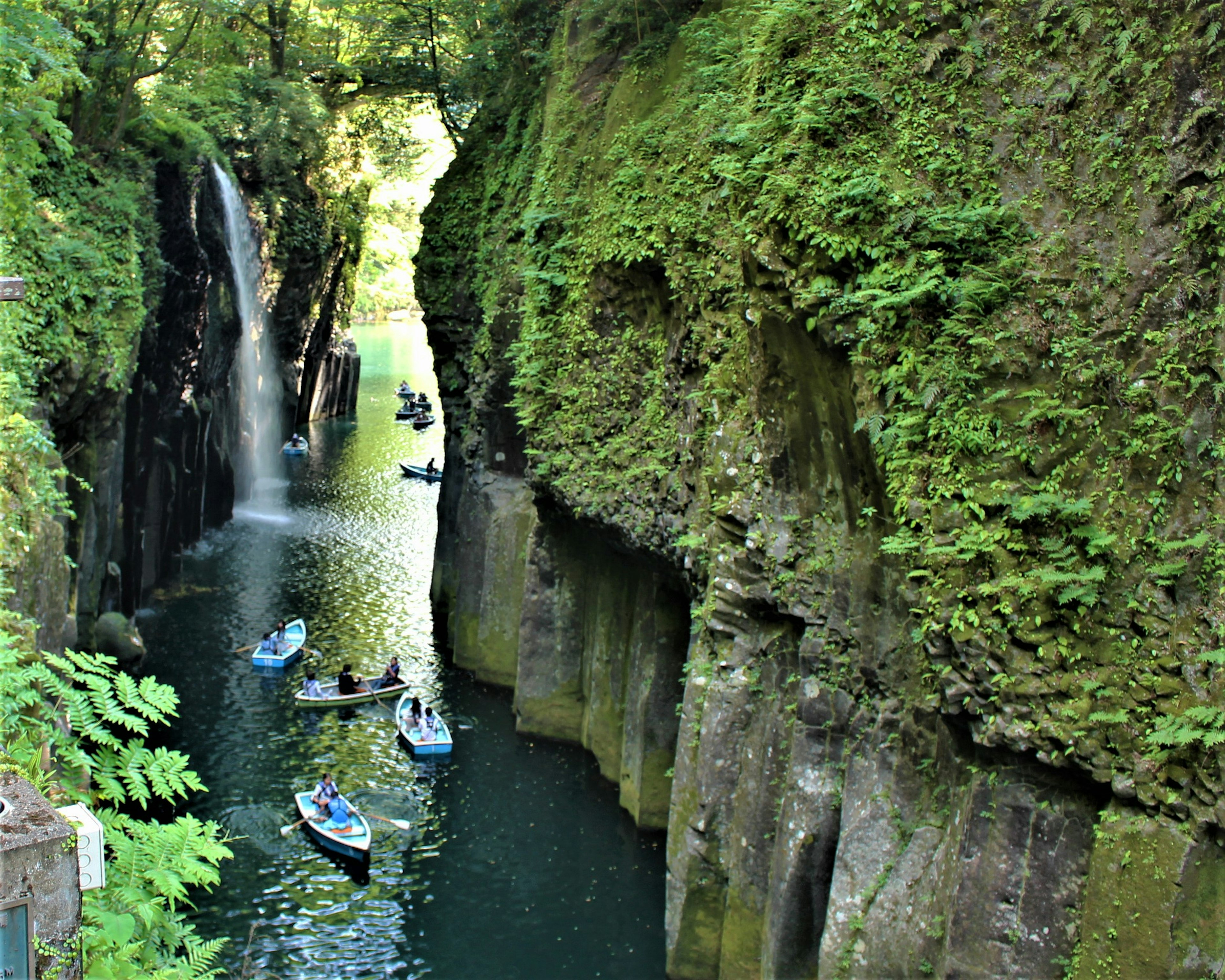 Un cañón verde con una cascada y pequeños botes en el agua