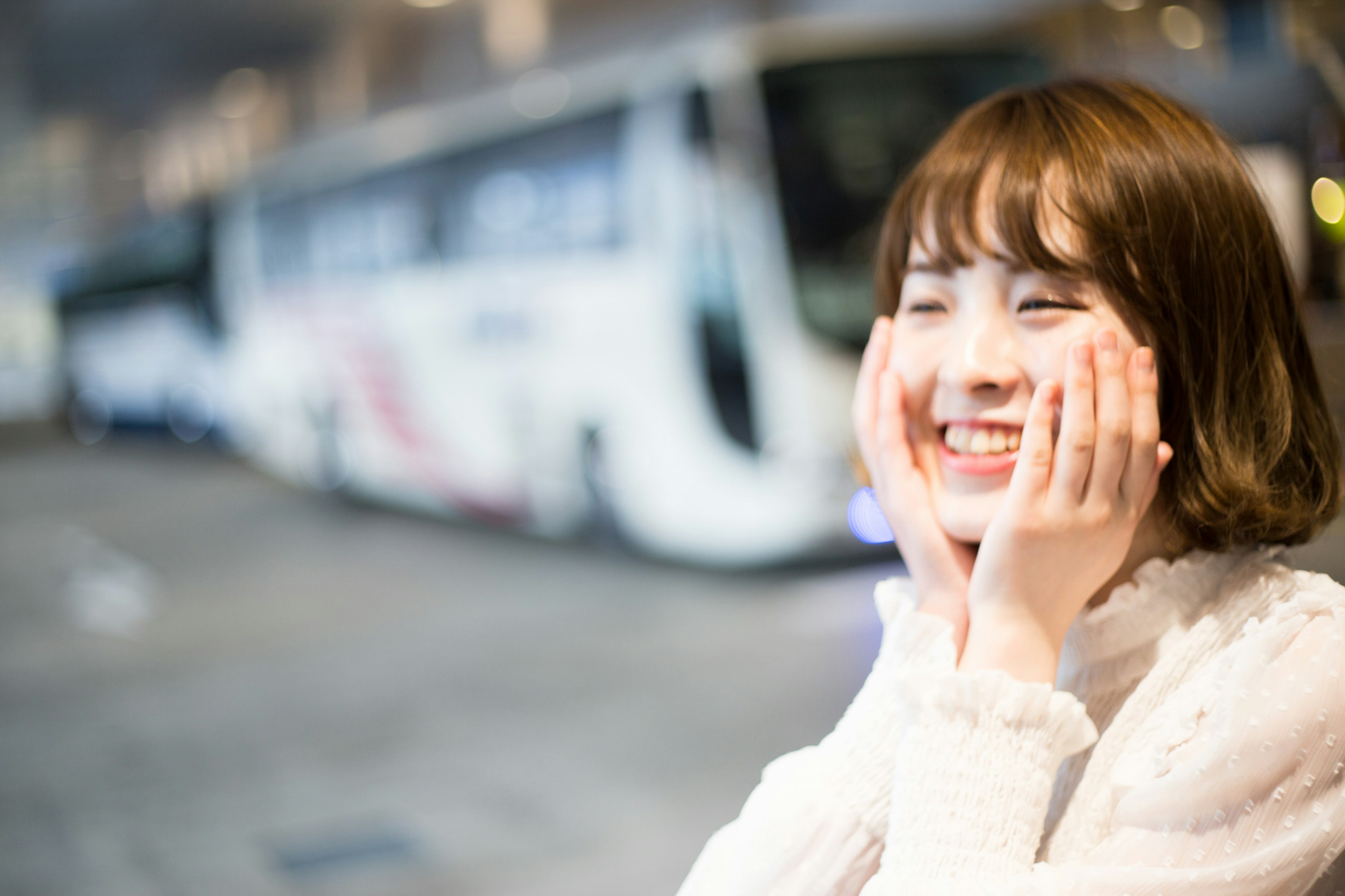 Femme souriante avec les mains sur les joues devant un bus