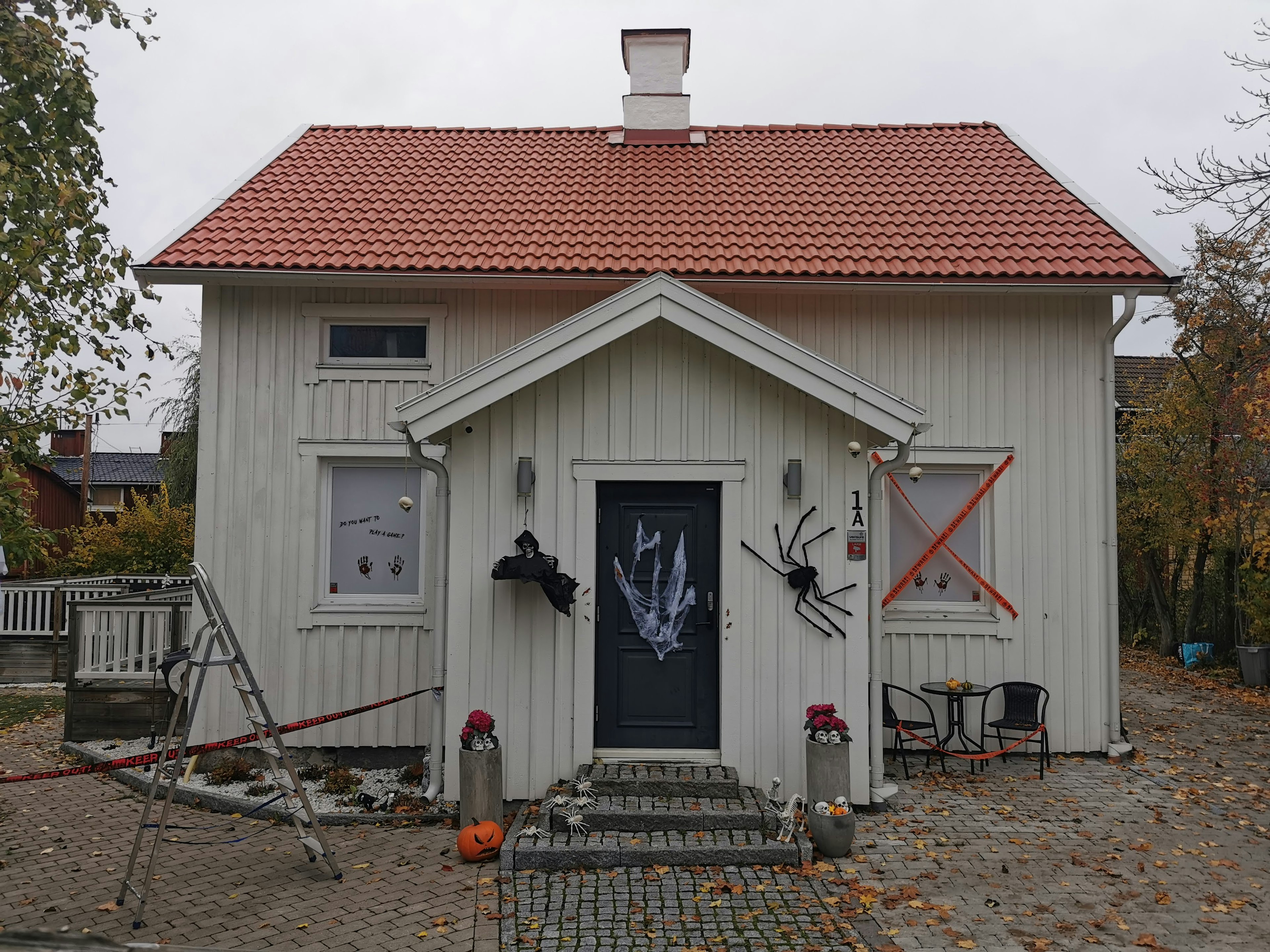 Una casa blanca con un techo rojo que presenta una entrada decorativa y decoraciones de Halloween