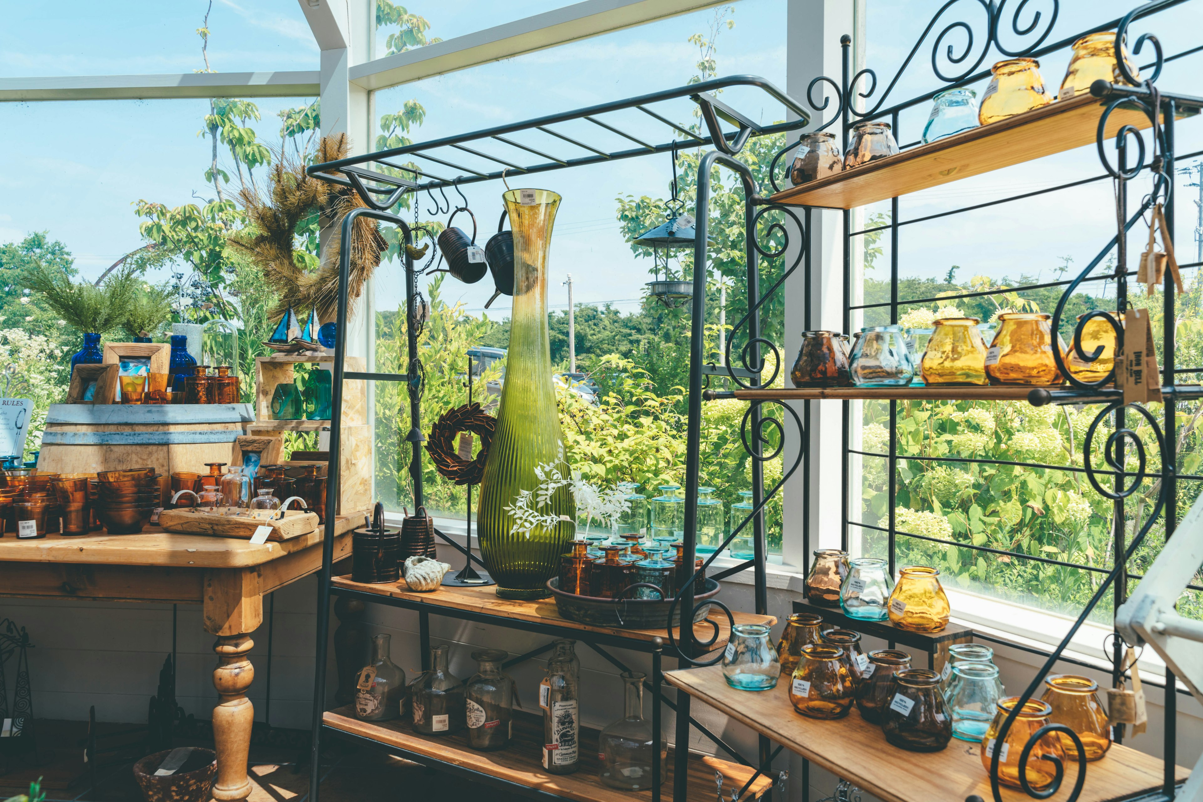 Bright glass greenhouse featuring decorative shelves with colorful bottles and vases