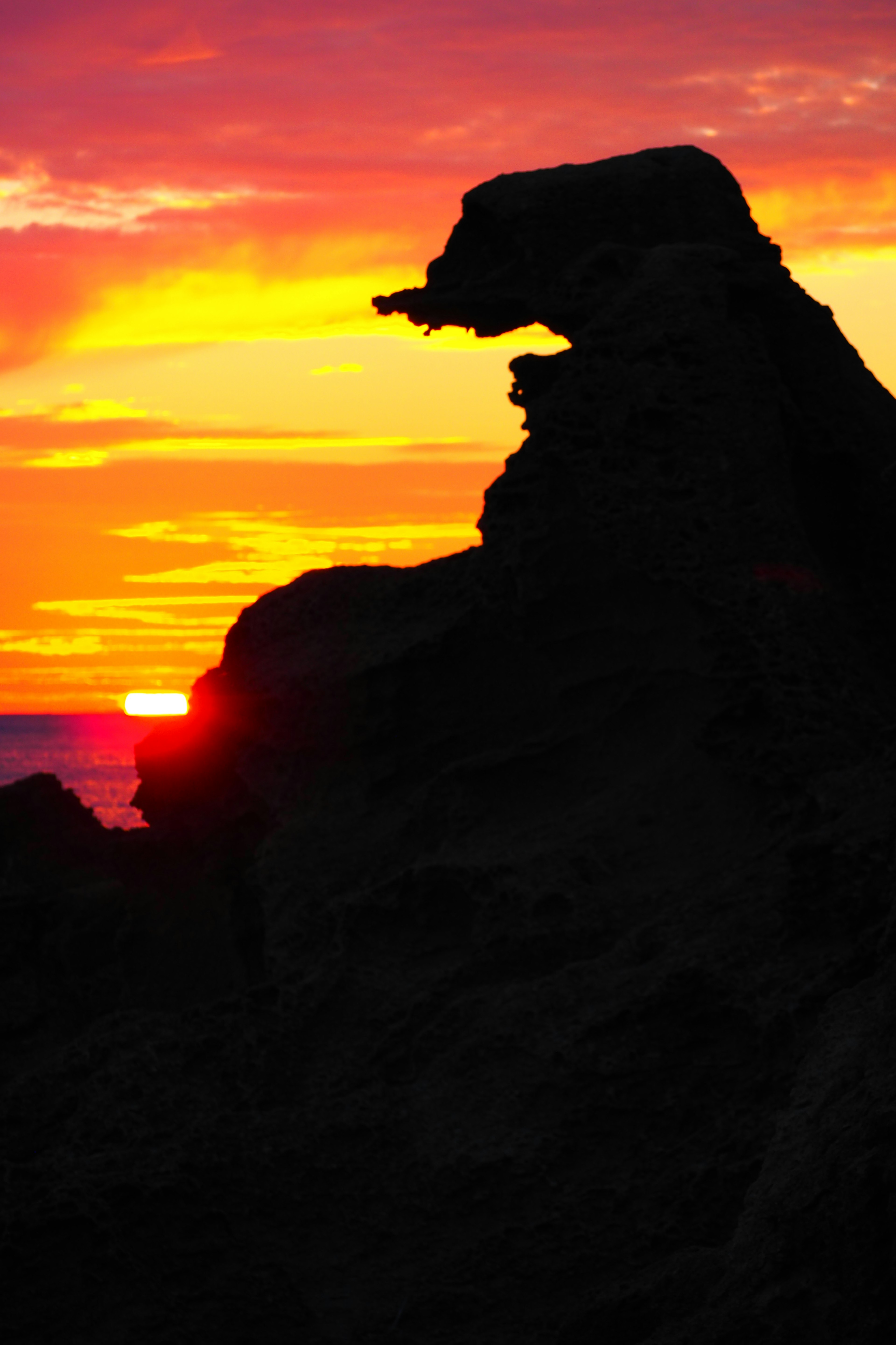 Silhouette einer Felsformation, die einem Hund ähnelt, vor einem lebhaften Sonnenuntergang