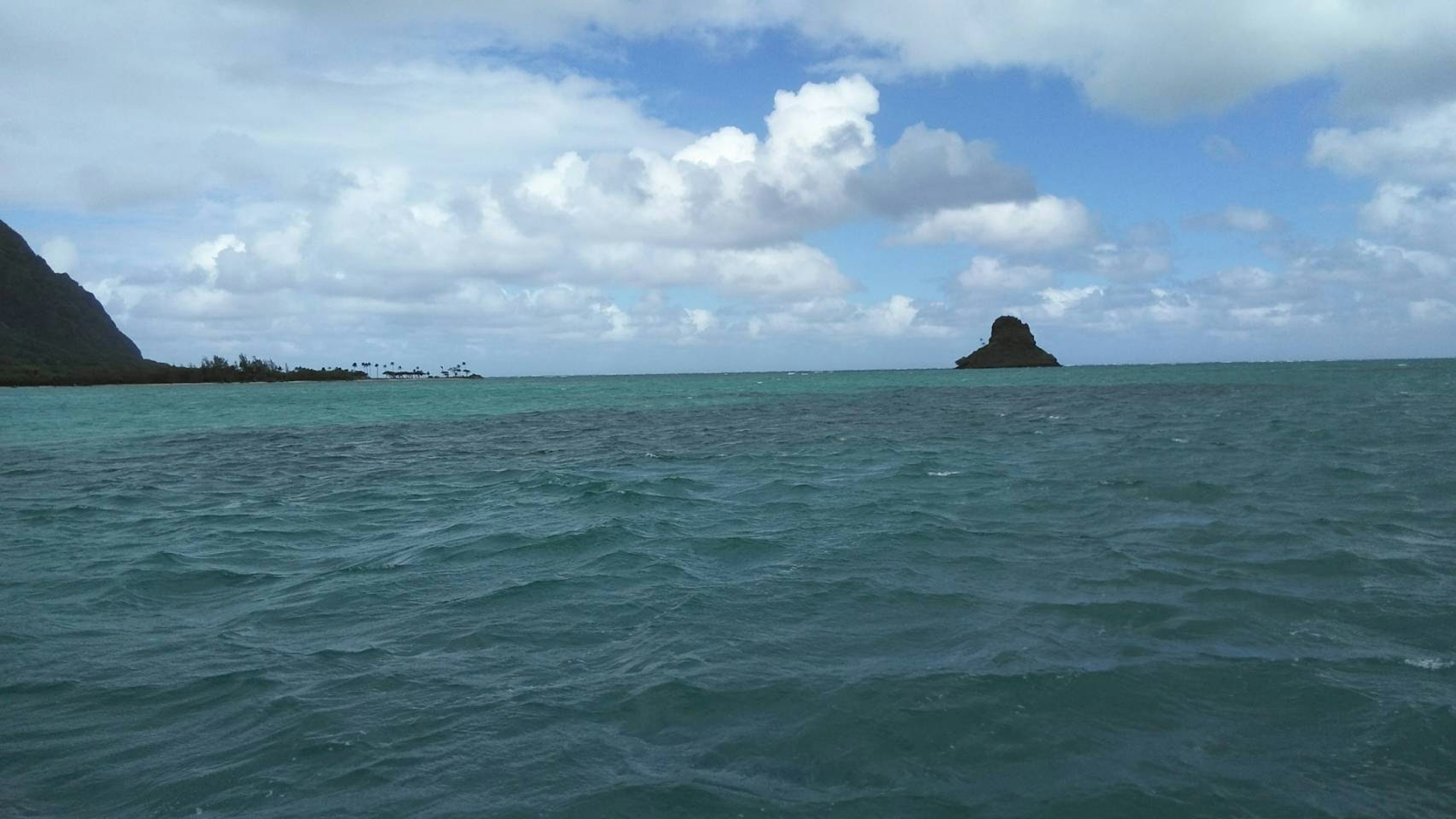 Scenic view of blue ocean with white clouds and a small island in the distance