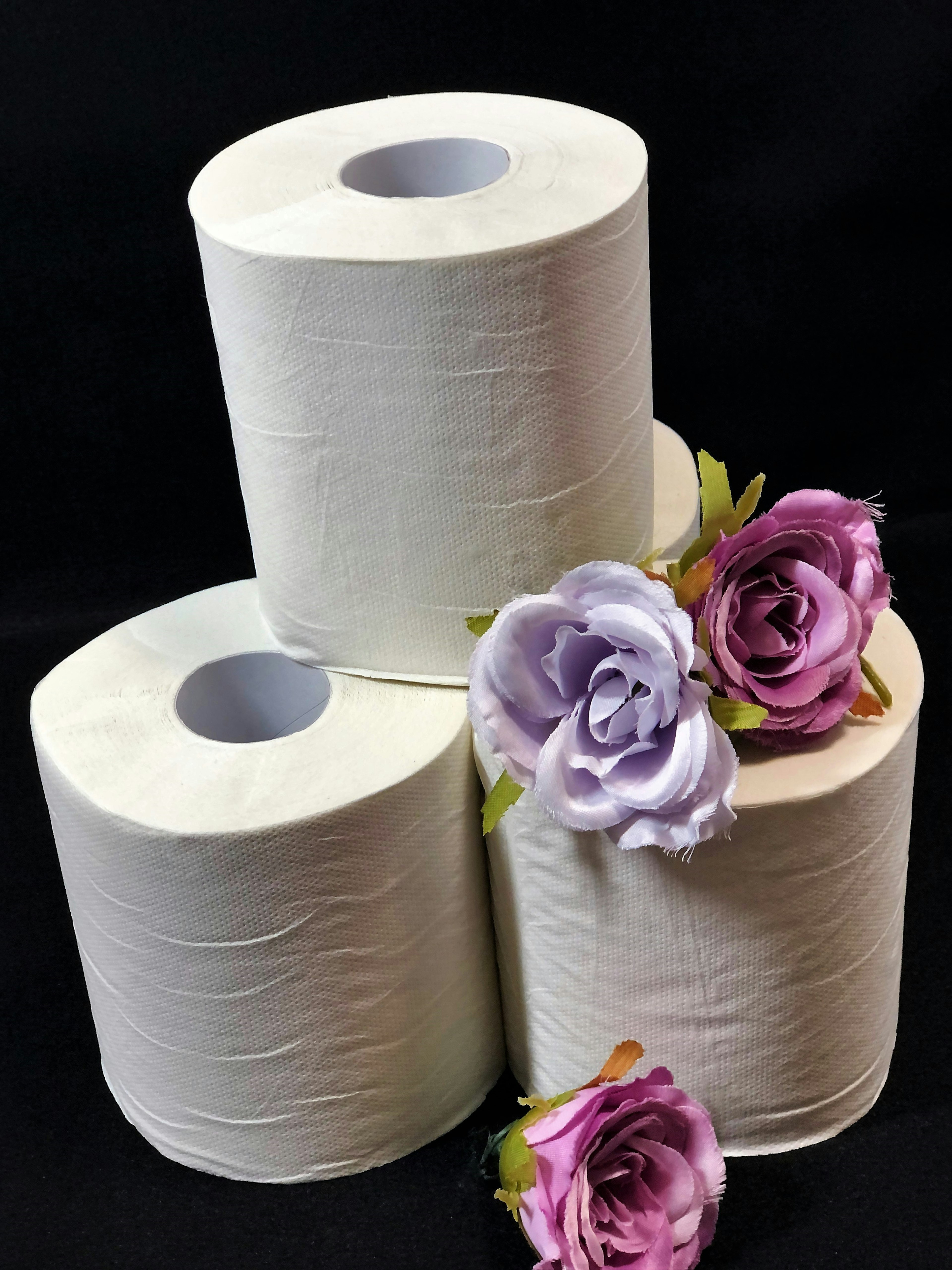 Trois rouleaux de papier toilette blanc avec des roses violettes autour d'eux