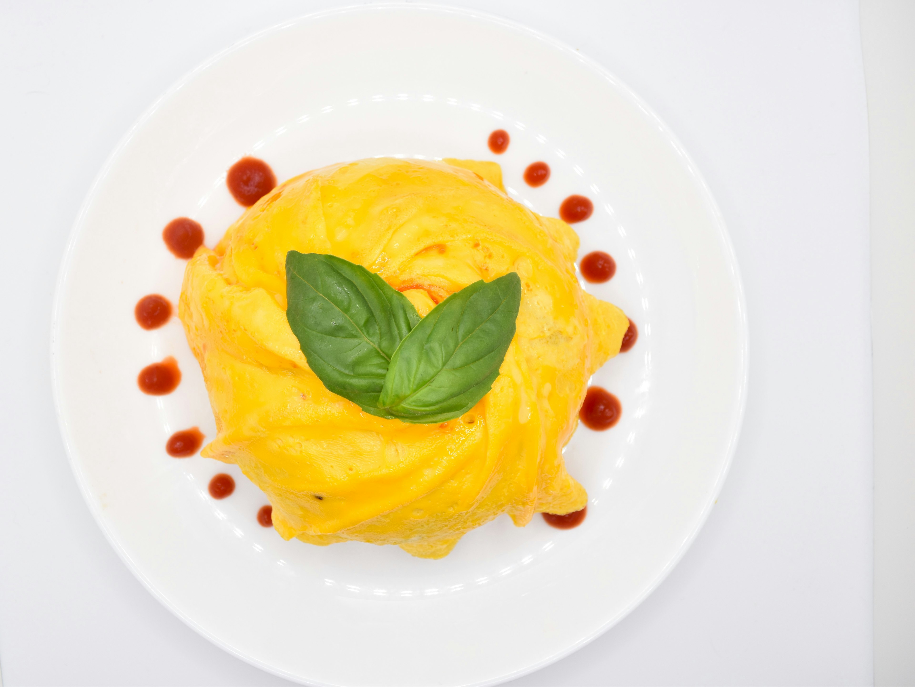 Un'omelette gialla guarnita con foglie di basilico fresco su un piatto bianco