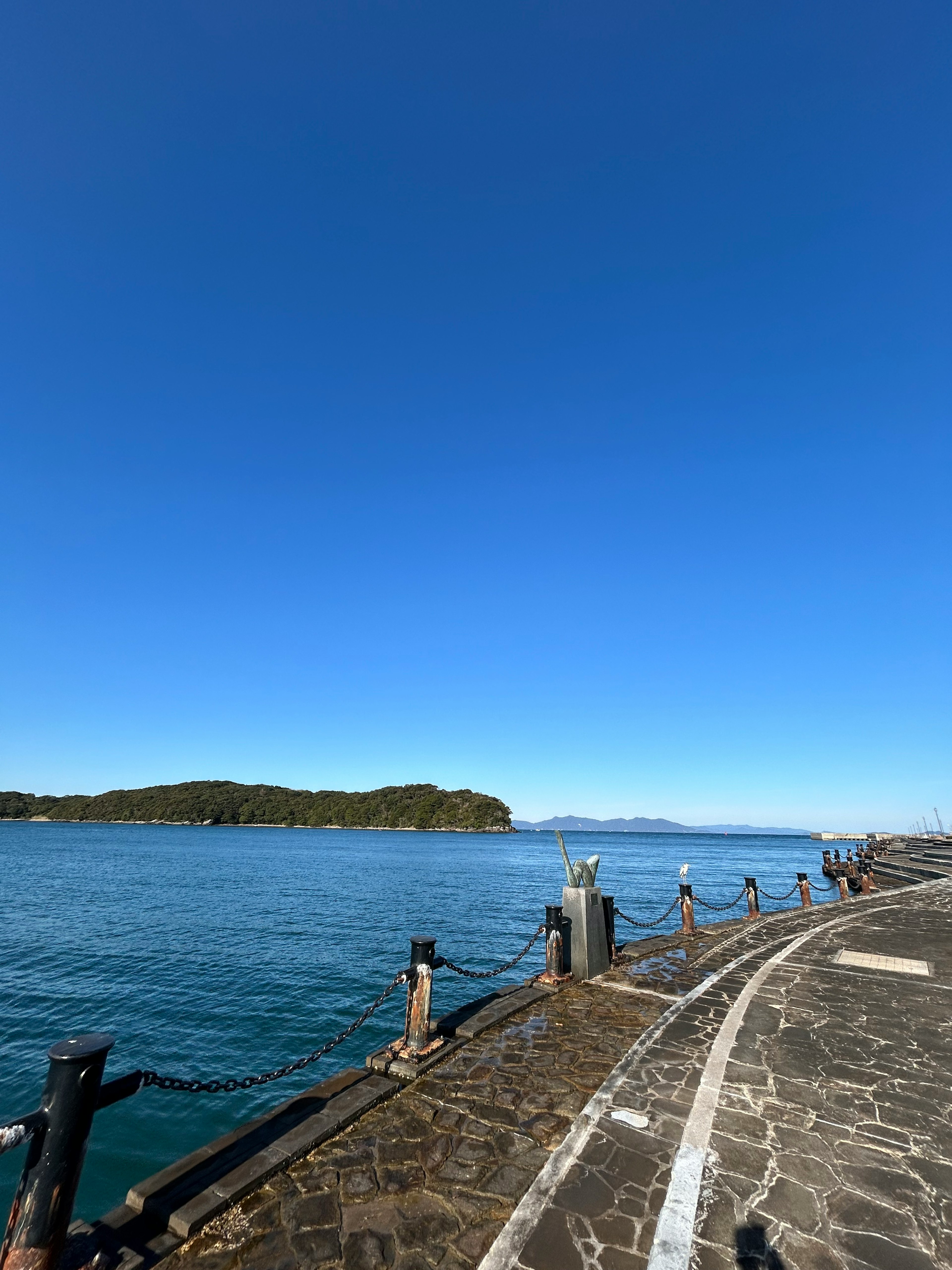 Ciel bleu clair sur une mer calme avec un quai en pierre et des rambardes