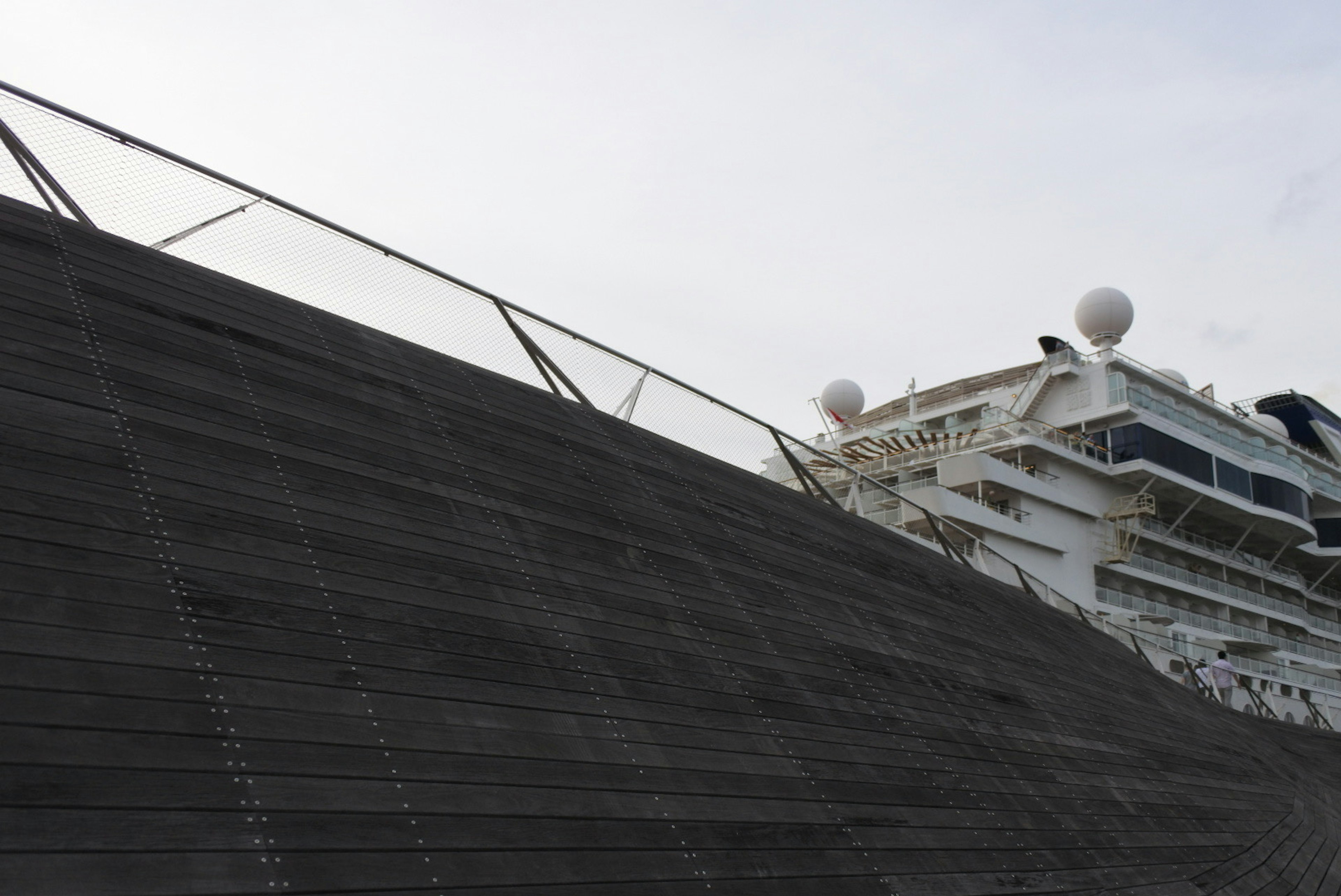 View of a cruise ship with a sloped surface and metal railing in the foreground