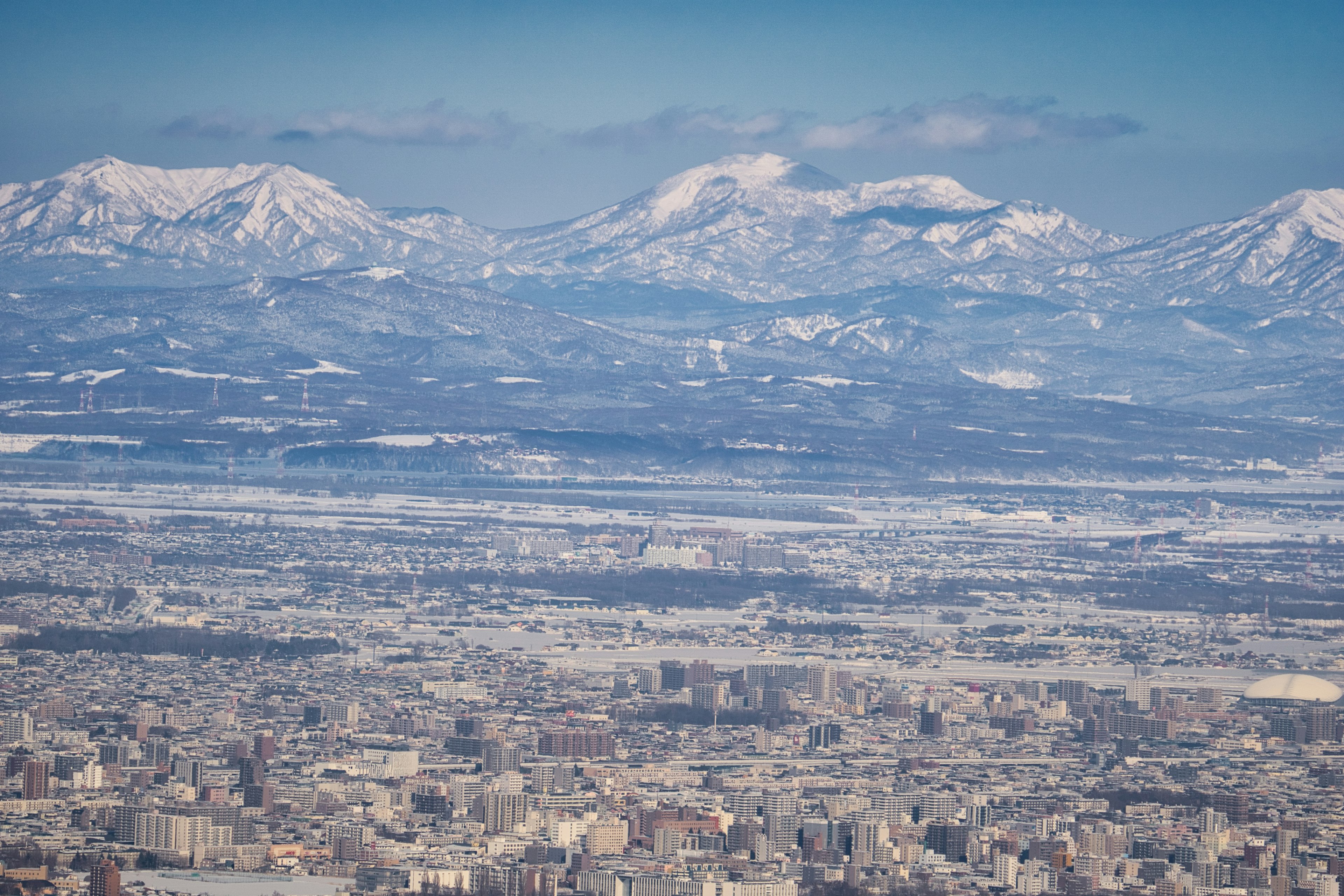 Montagne innevate che sovrastano un vasto paesaggio urbano