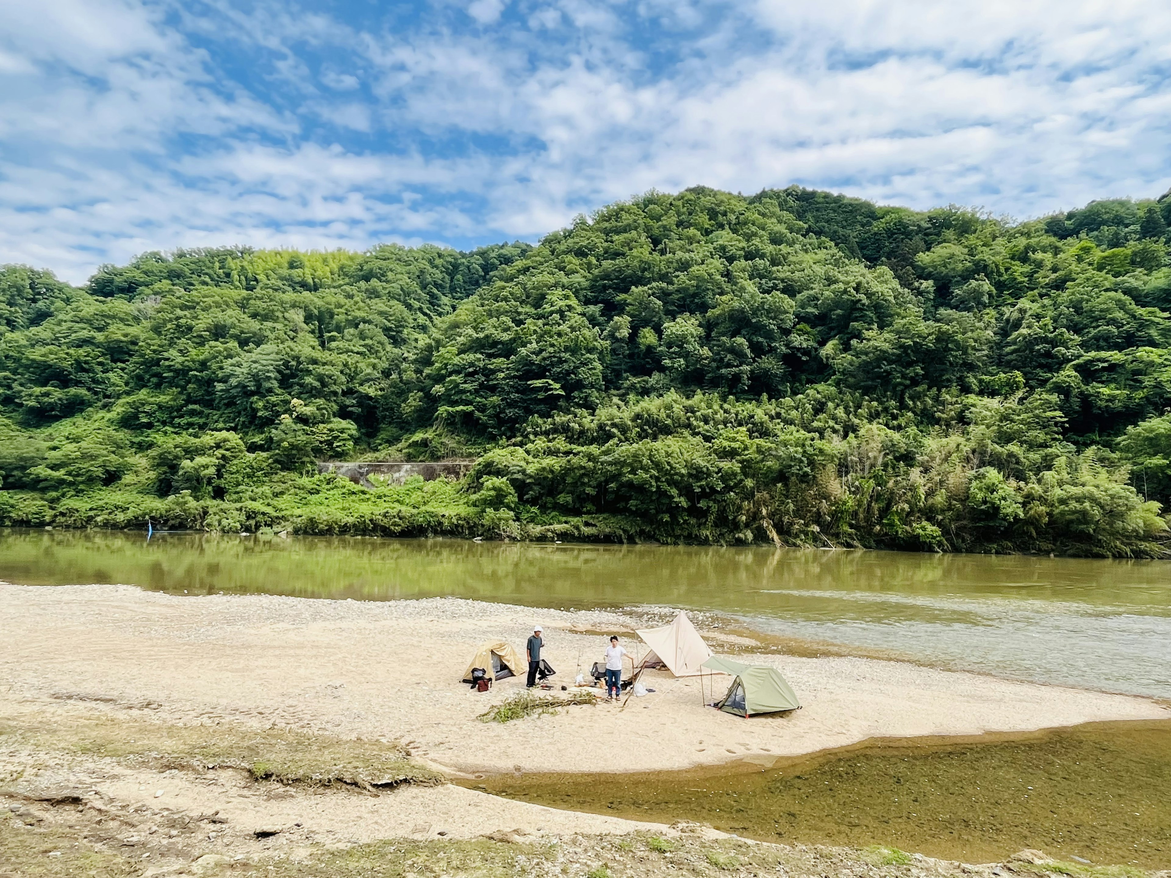 Persone che montano tende sulla riva del fiume con colline verdi