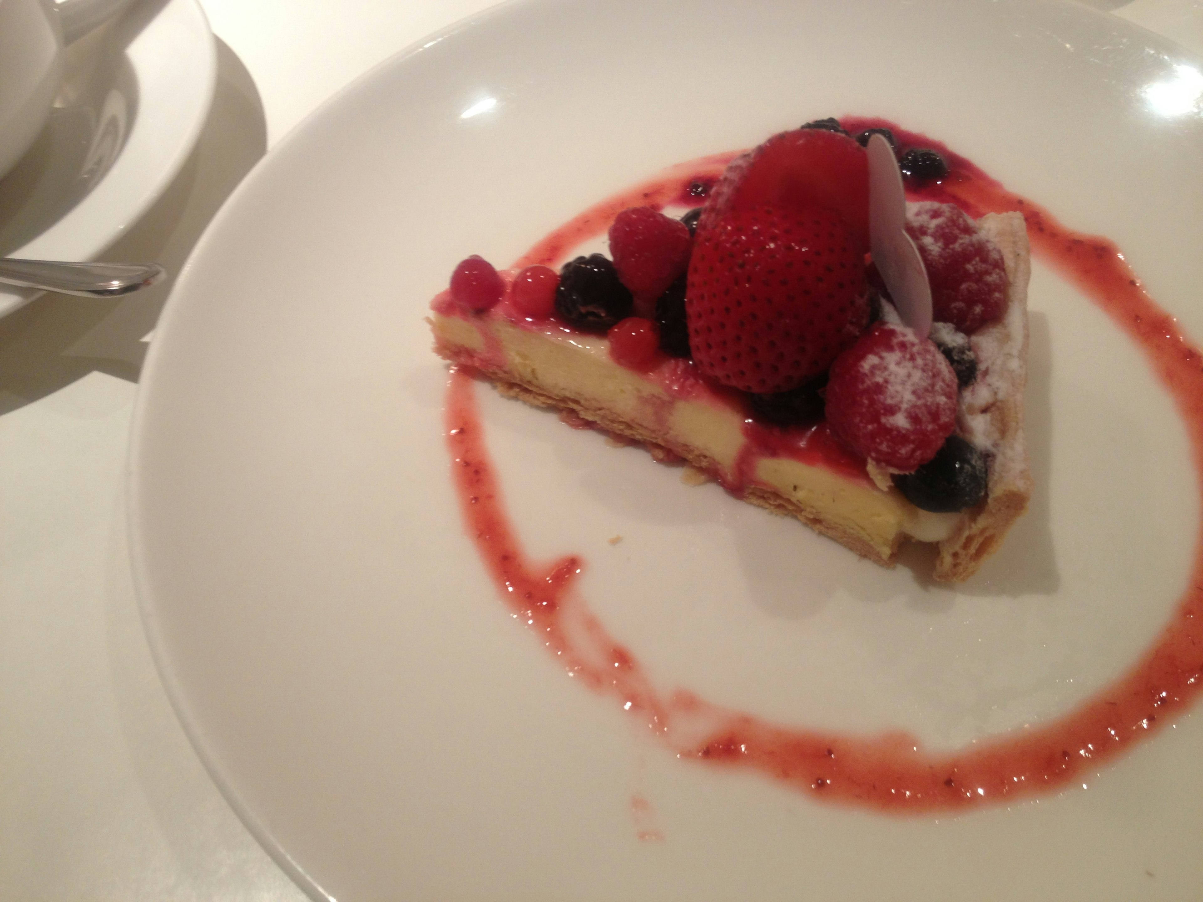 A slice of delicious berry tart on a white plate with red sauce drizzled around it