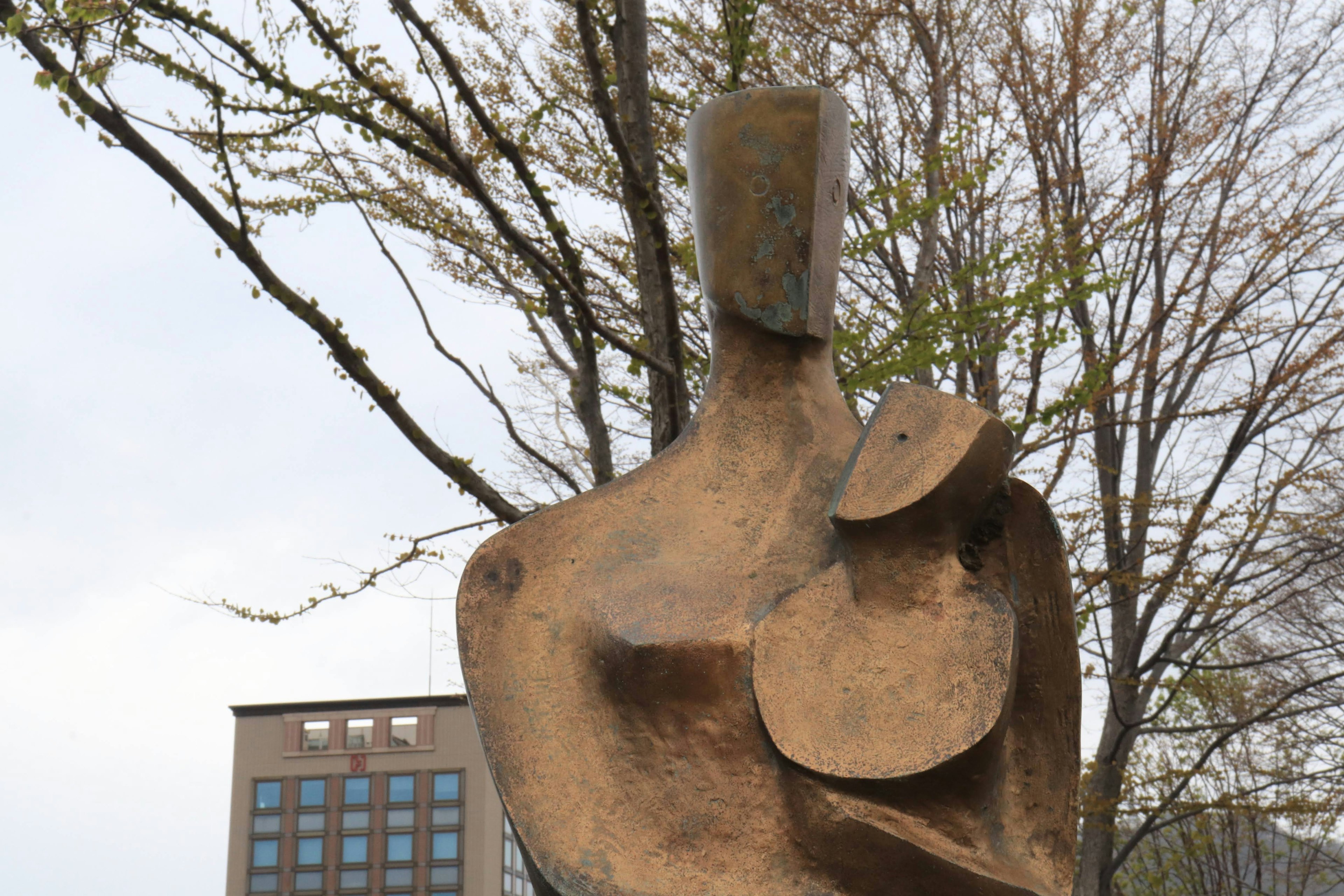 Sculpture abstraite d'une figure tenant un enfant entourée d'arbres