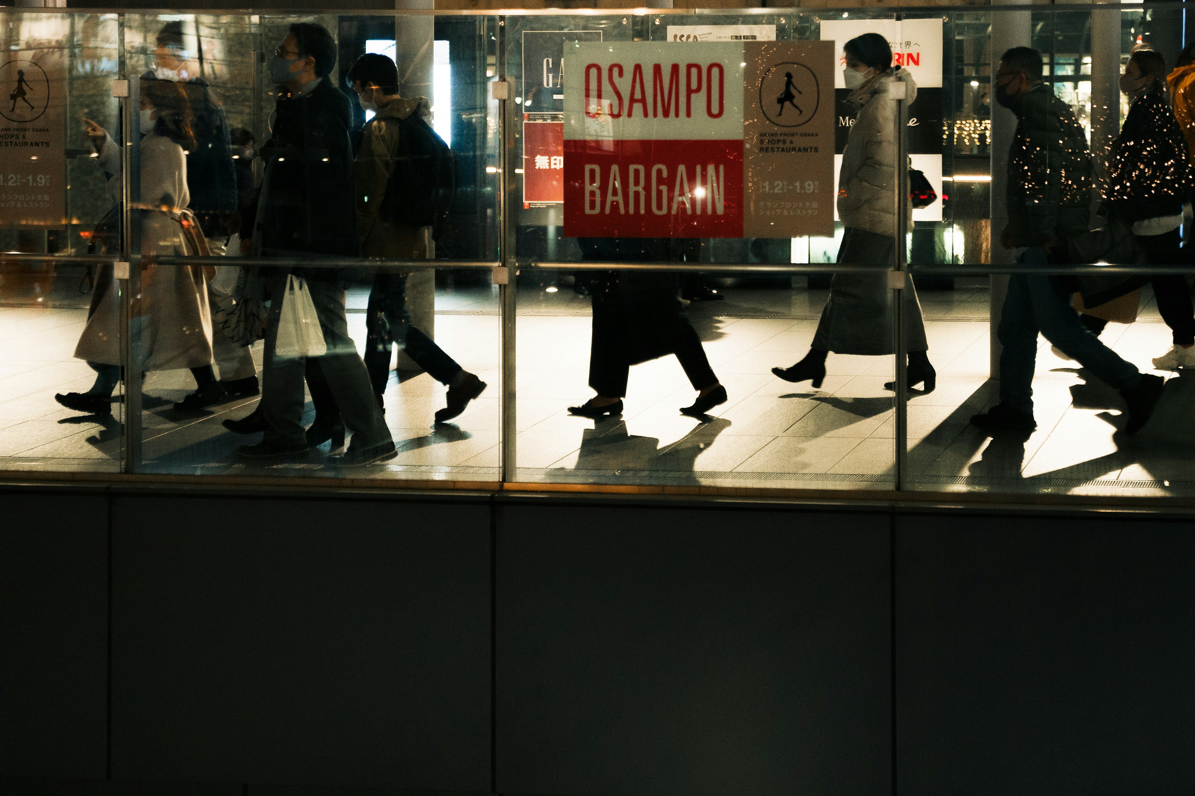 Personas caminando en un área comercial por la noche con un cartel de oferta