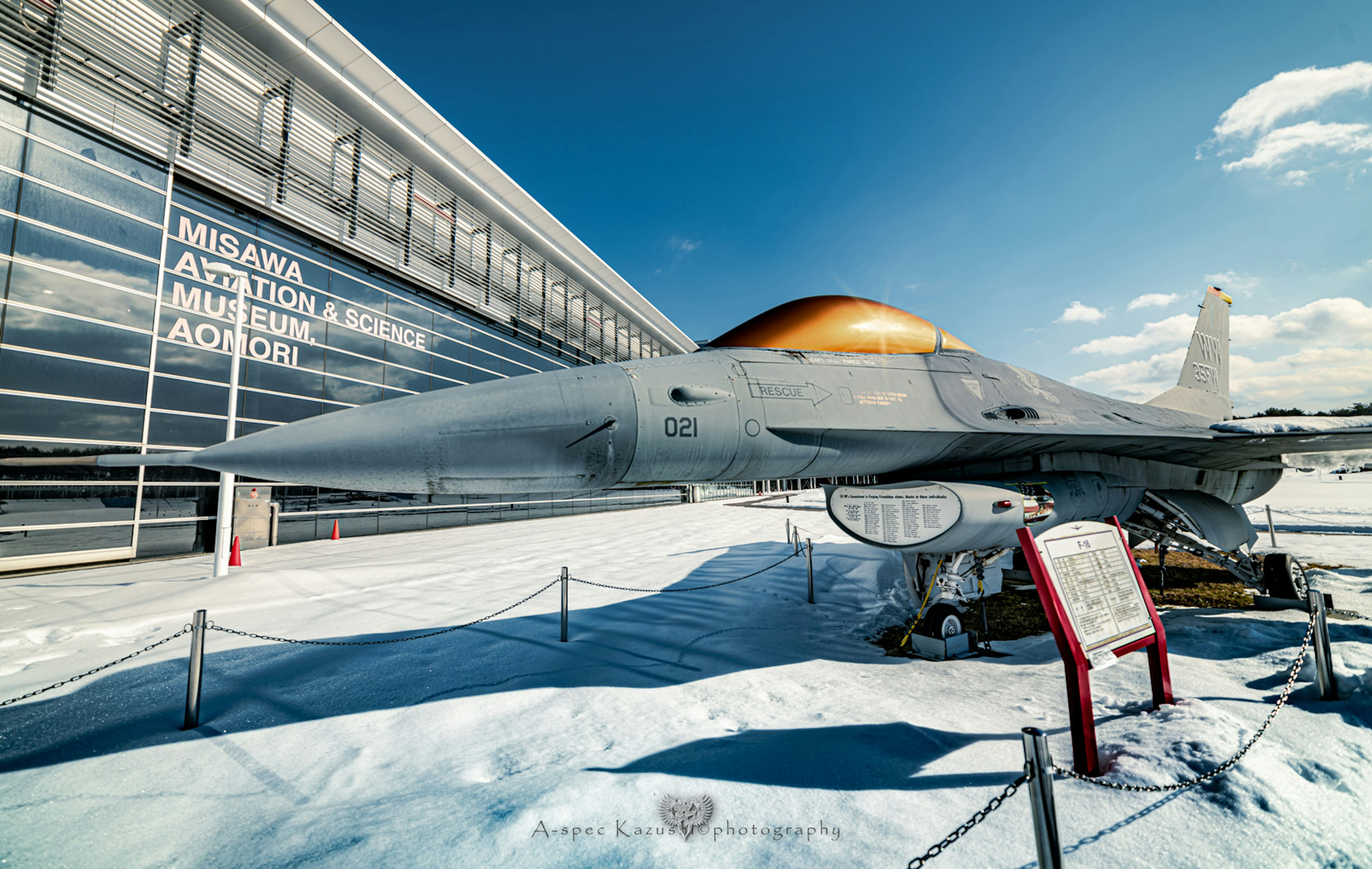 Fighter jet displayed on snow with modern building in background