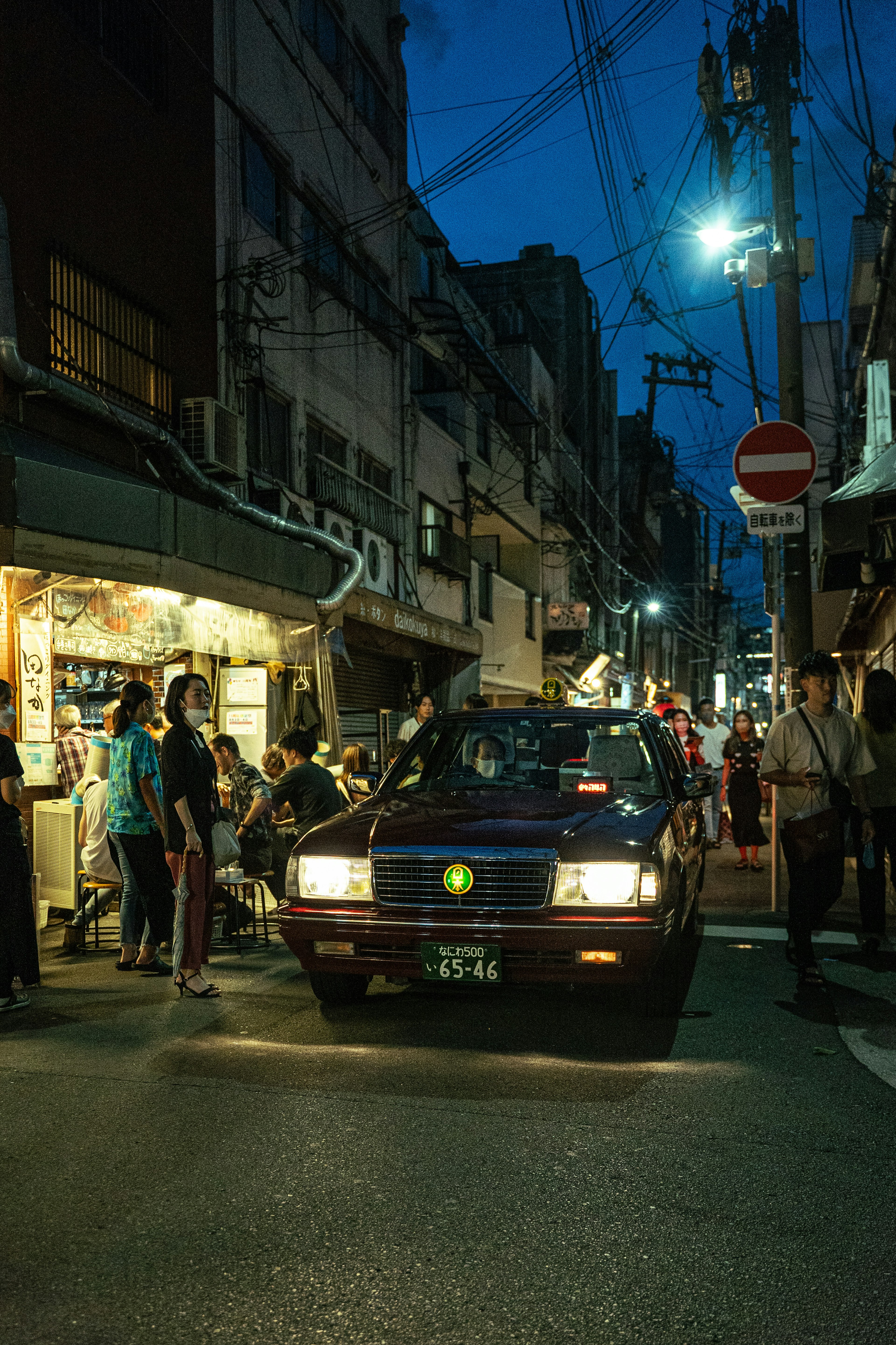 แท็กซี่ในถนนที่พลุกพล่านในตอนกลางคืนพร้อมผู้คนและร้านค้า