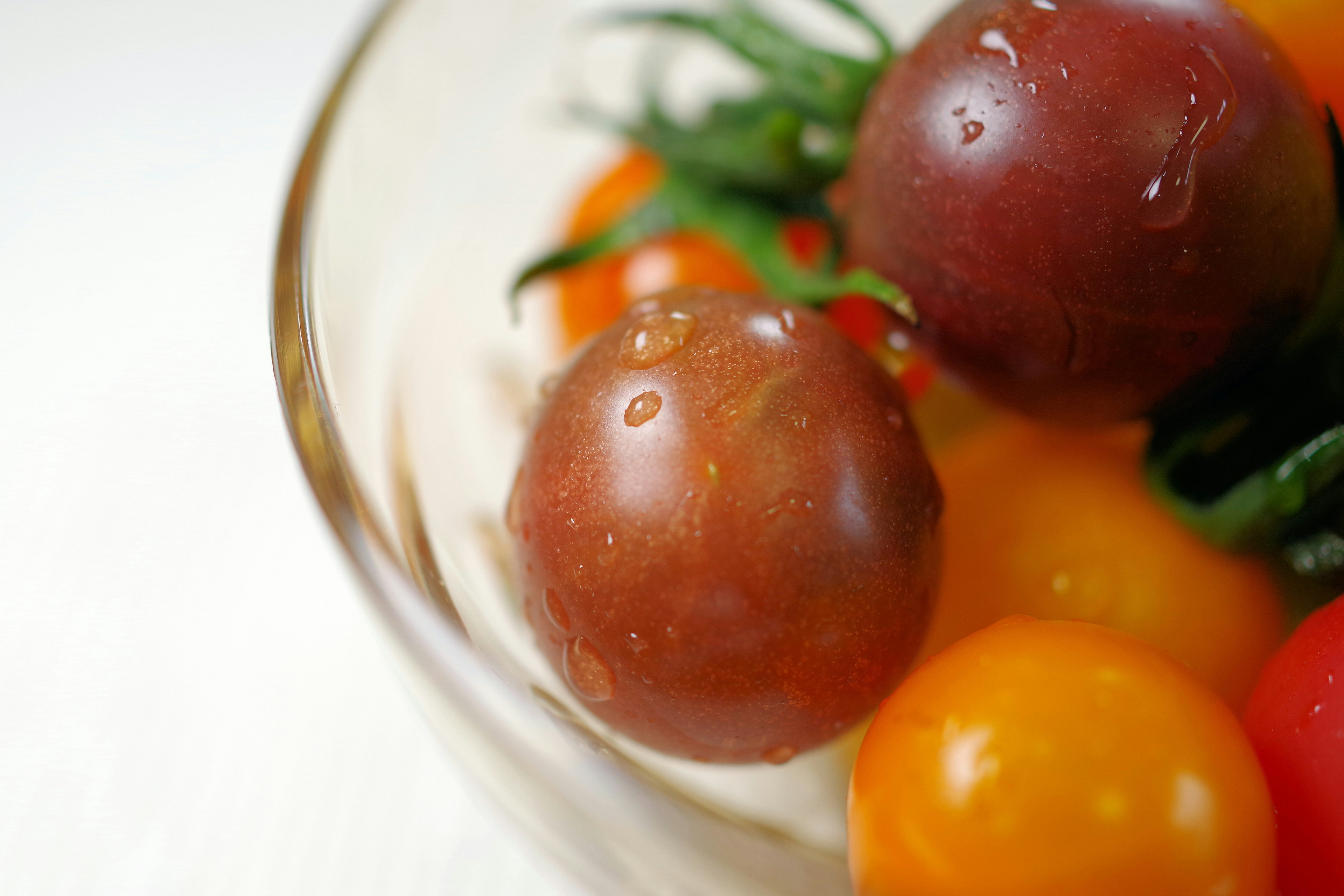 Tomates cherry coloridas con gotas de agua en un tazón transparente