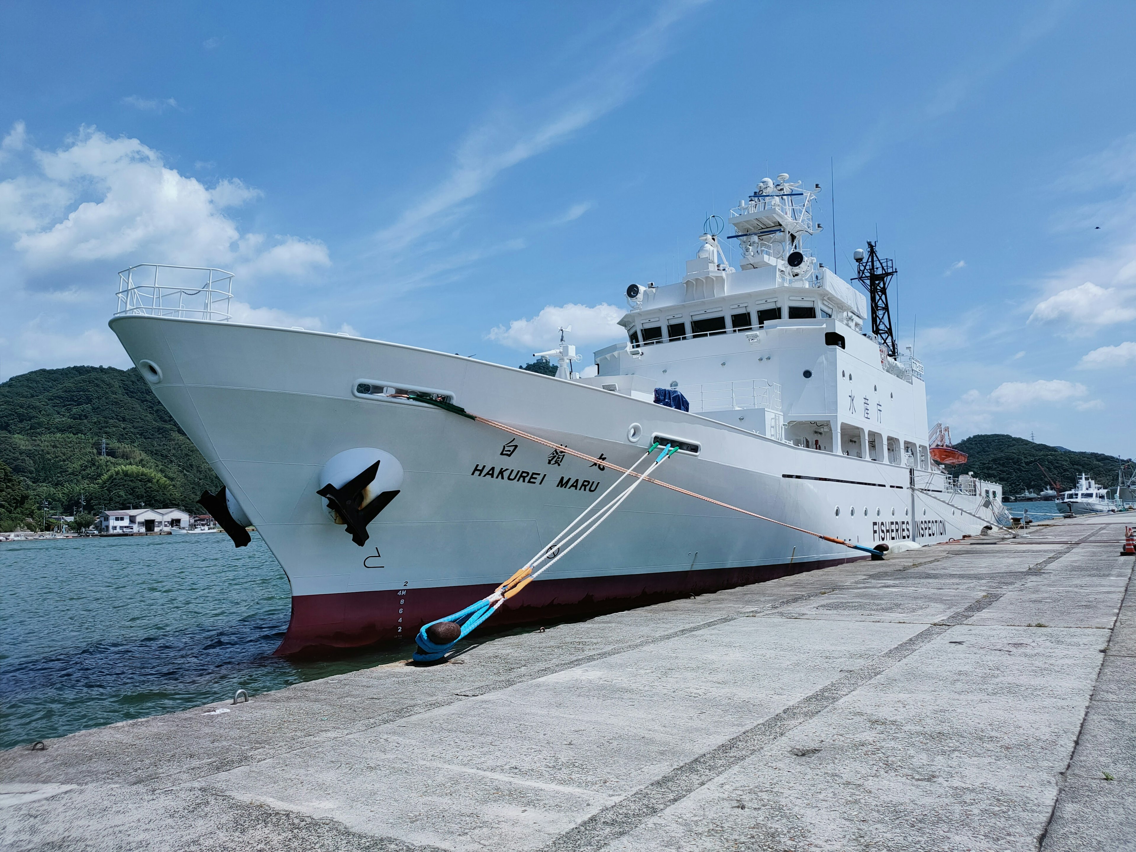 Kapal penelitian putih besar berlabuh di pelabuhan dengan langit biru dan gunung di latar belakang