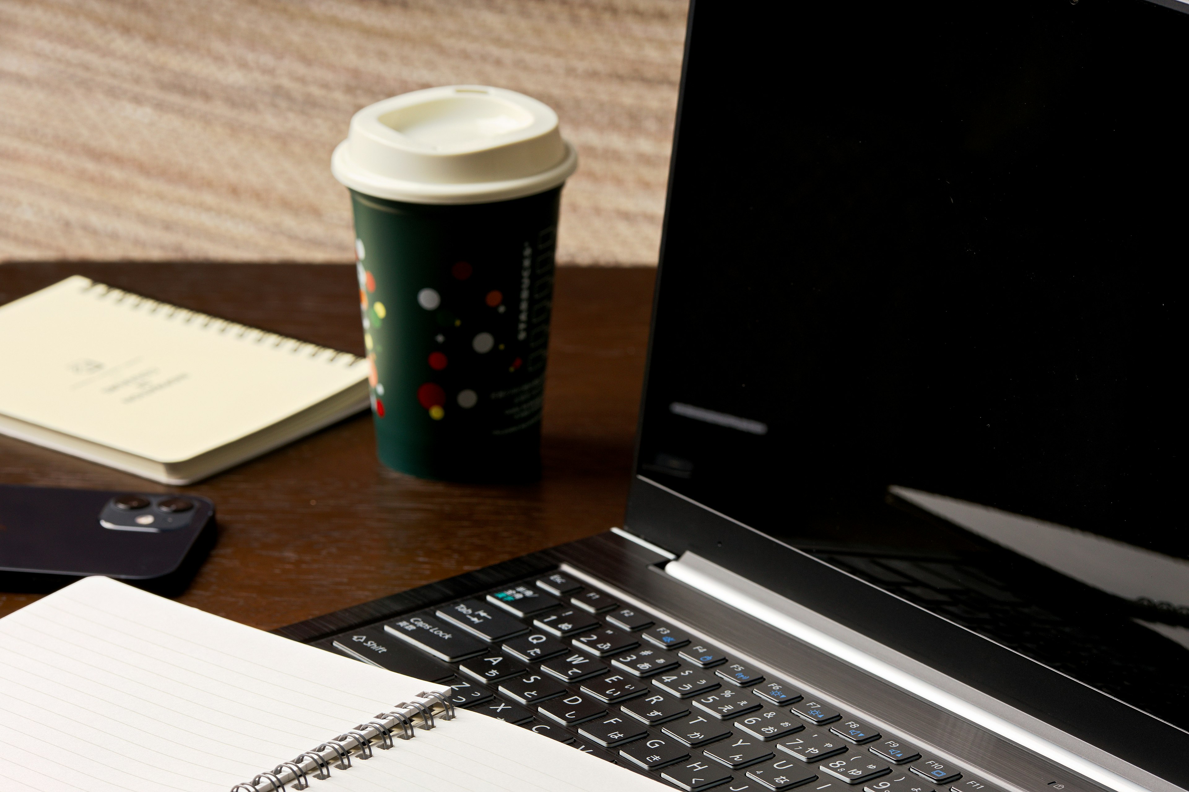 Desk scene featuring a black laptop next to a coffee cup and a notepad