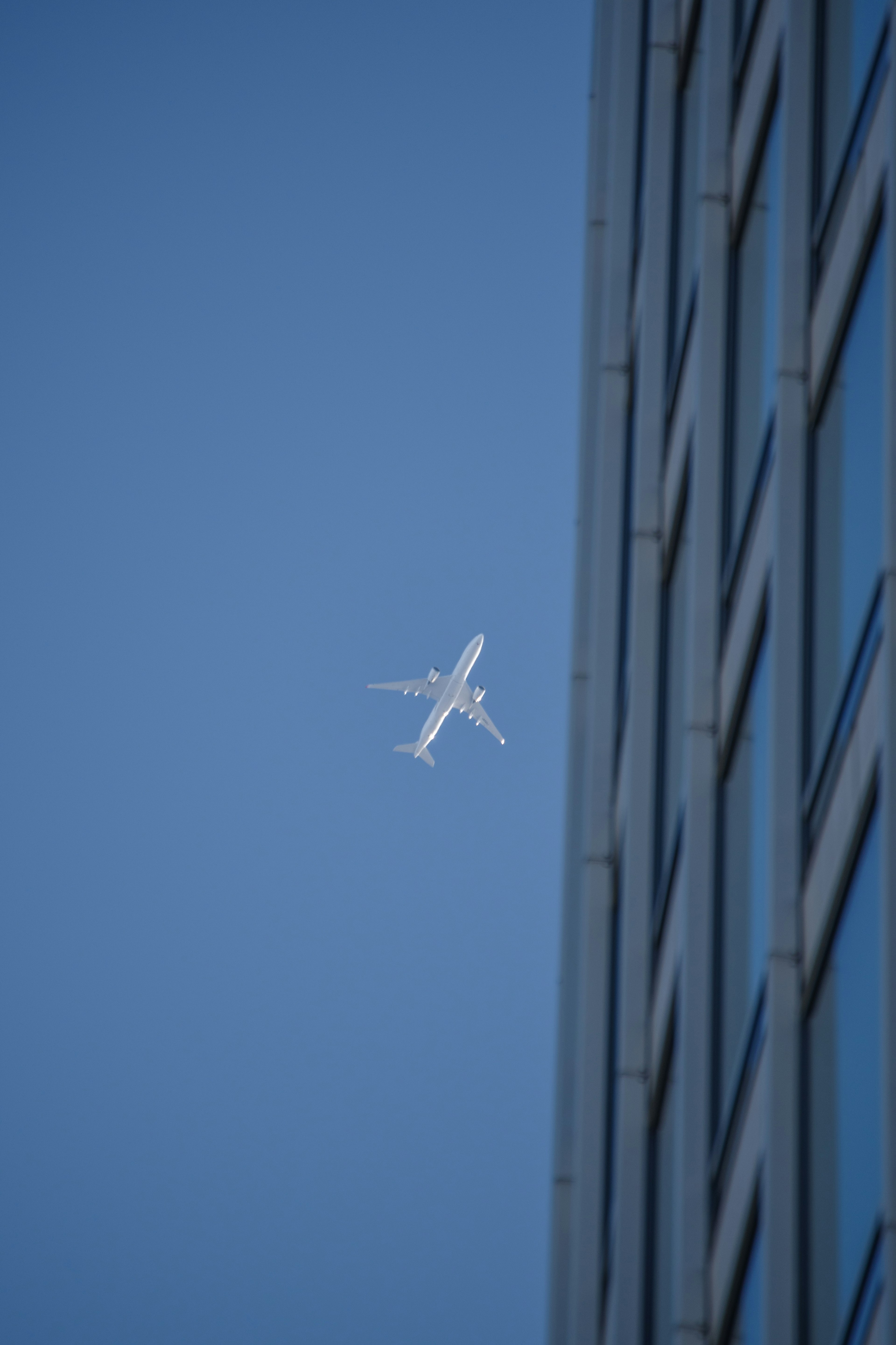 Airplane flying in blue sky next to building