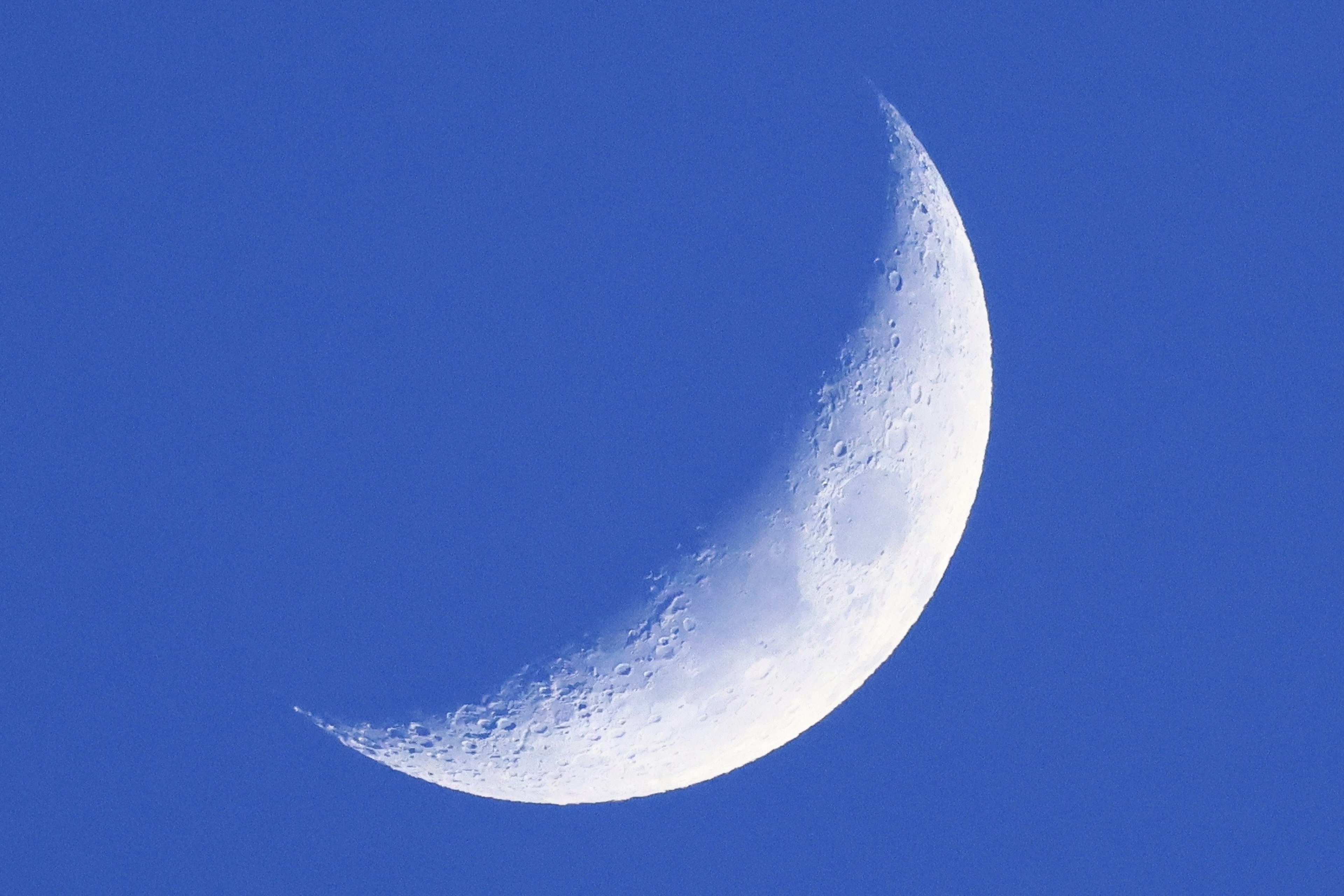 A thin crescent moon against a blue sky