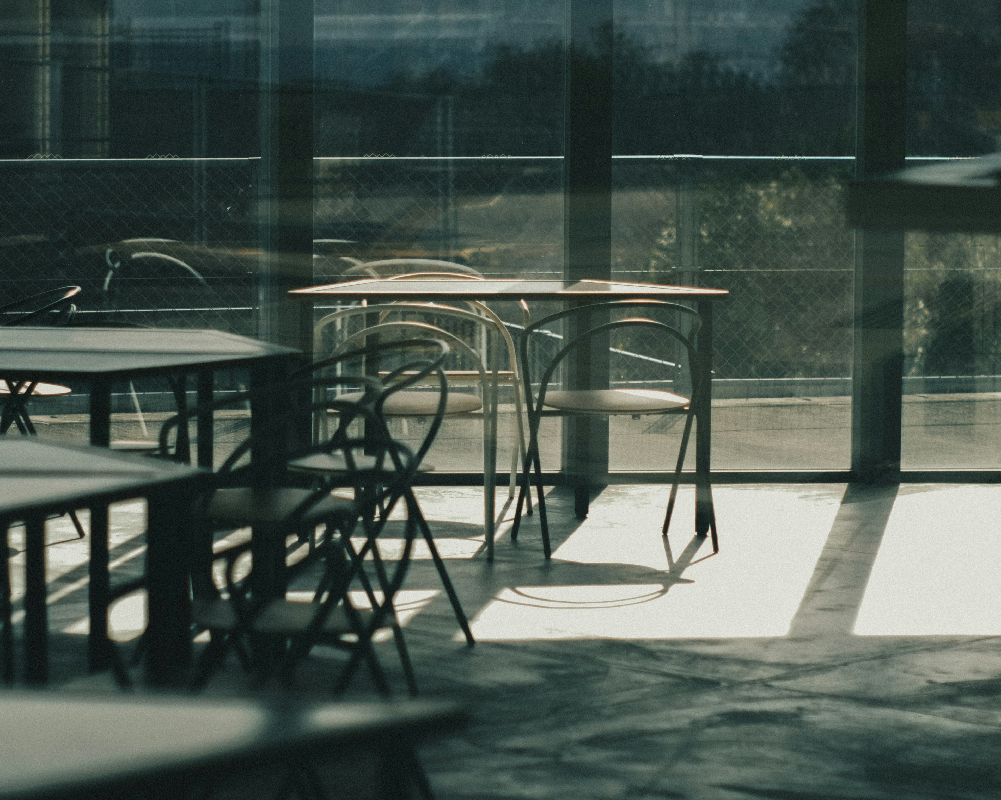 Interior of a quiet cafe with tables and chairs illuminated by natural light from large windows