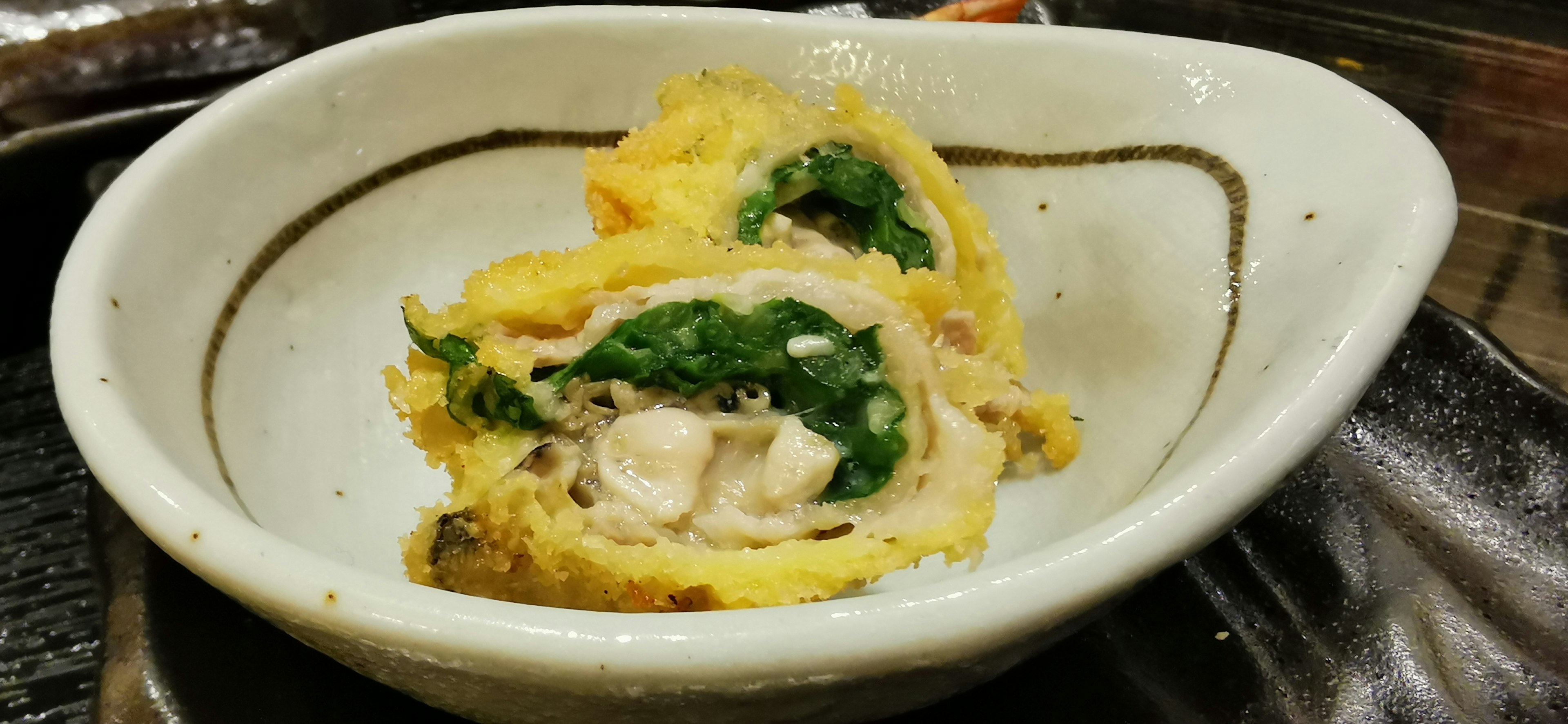 Dish featuring rolled egg with spinach served in a white bowl