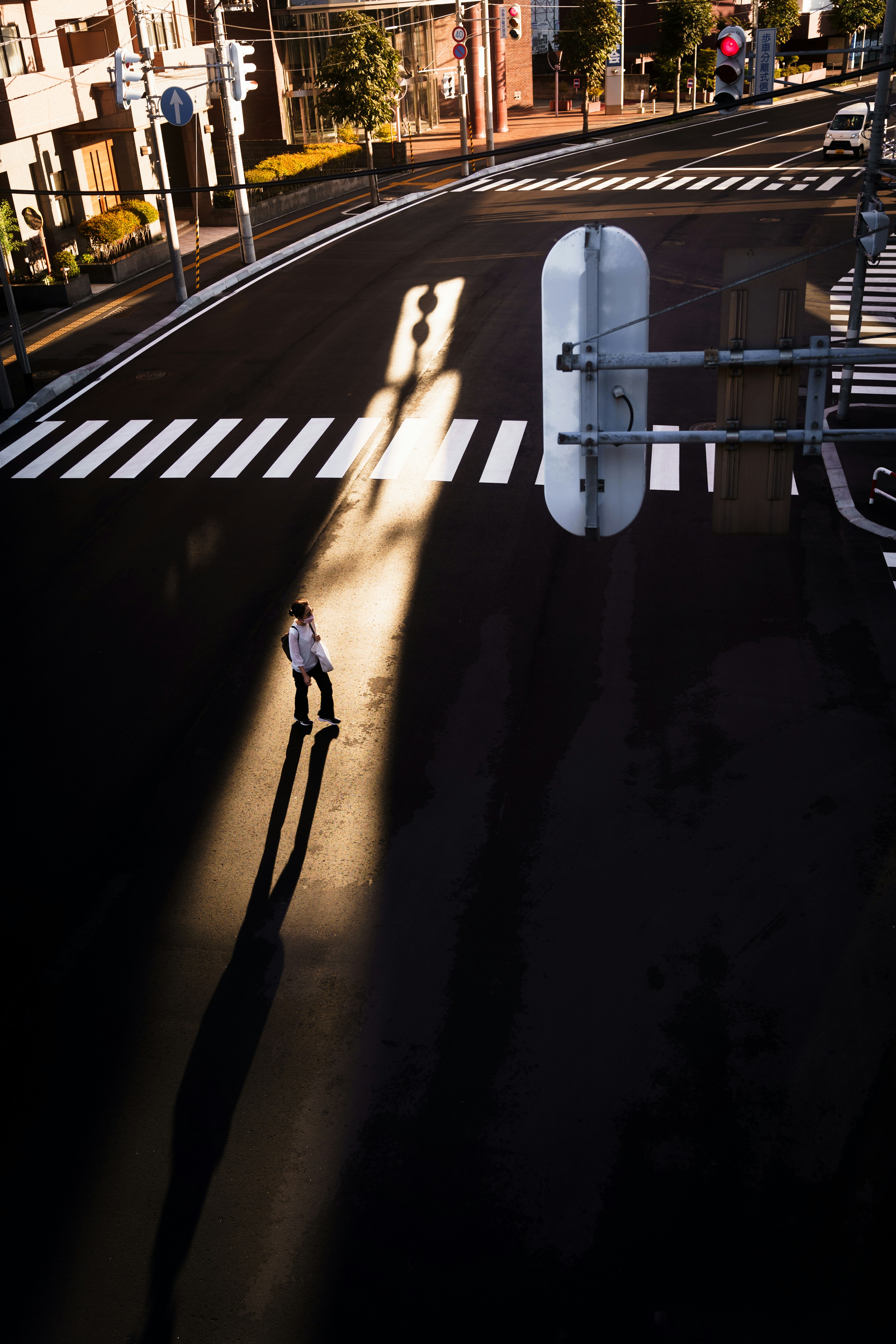 A solitary figure standing at an intersection casting a long shadow