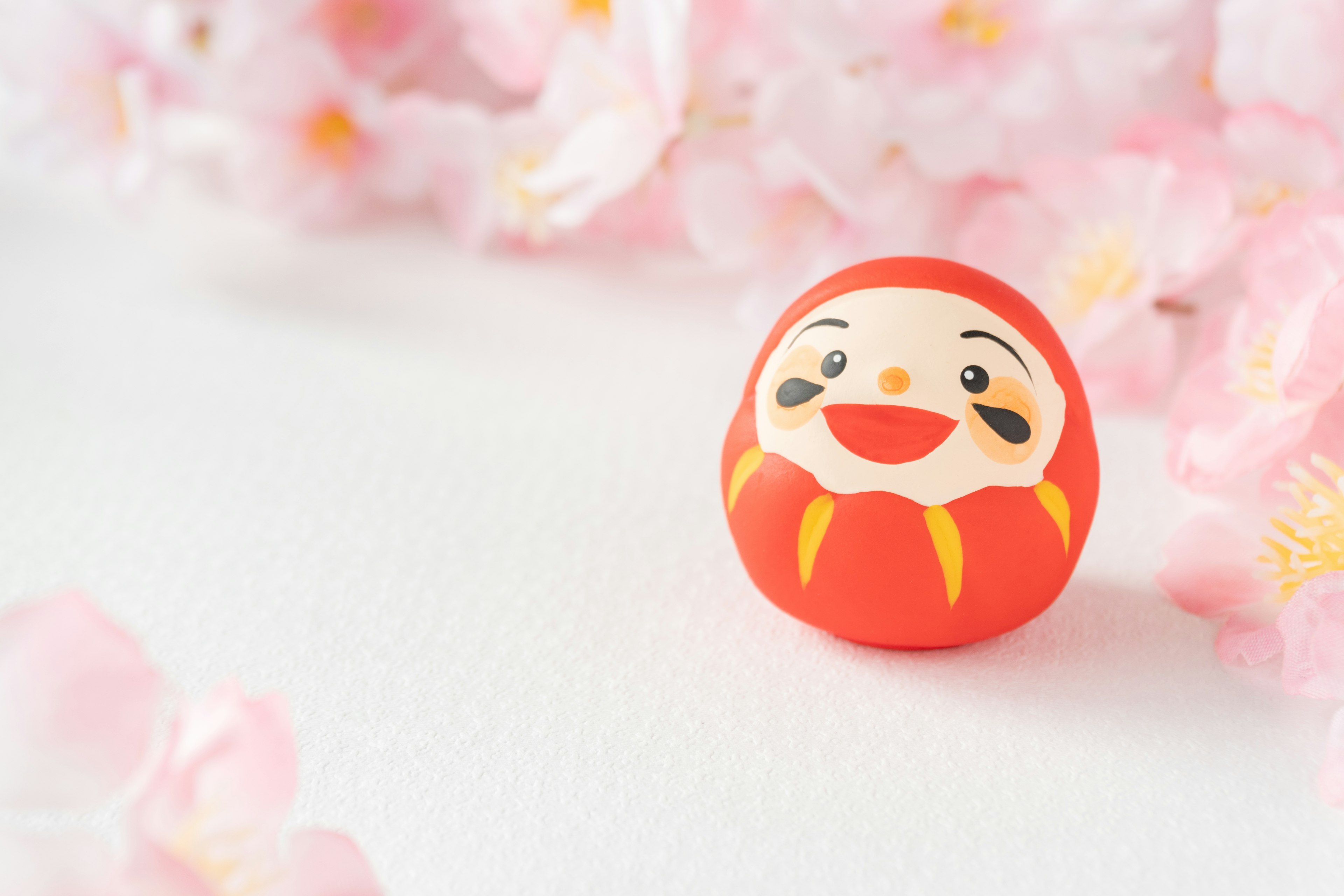 Red daruma doll placed in front of pink flowers