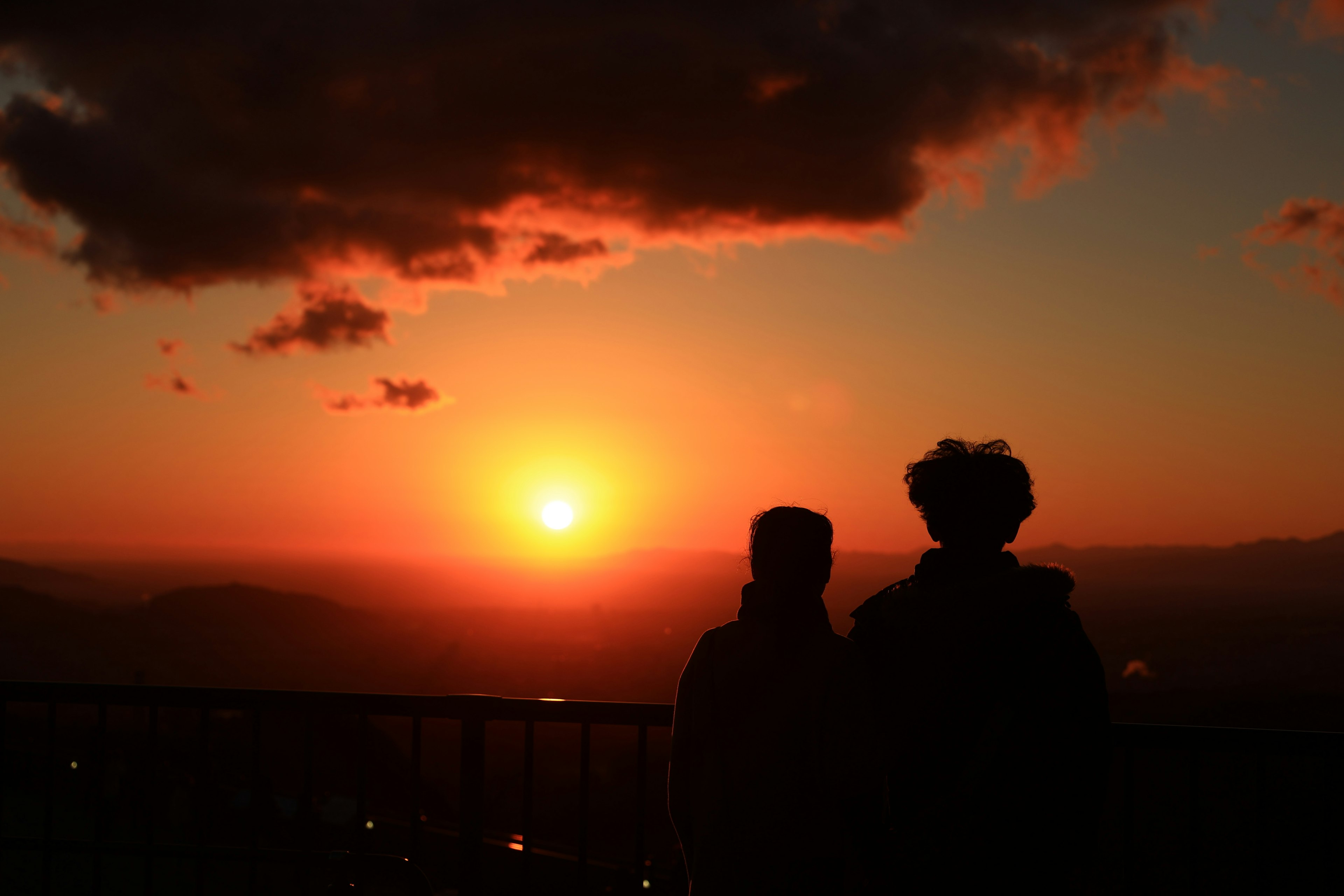 Silhouette von zwei Personen, die einen Sonnenuntergang mit einem schönen orangefarbenen Himmel betrachten