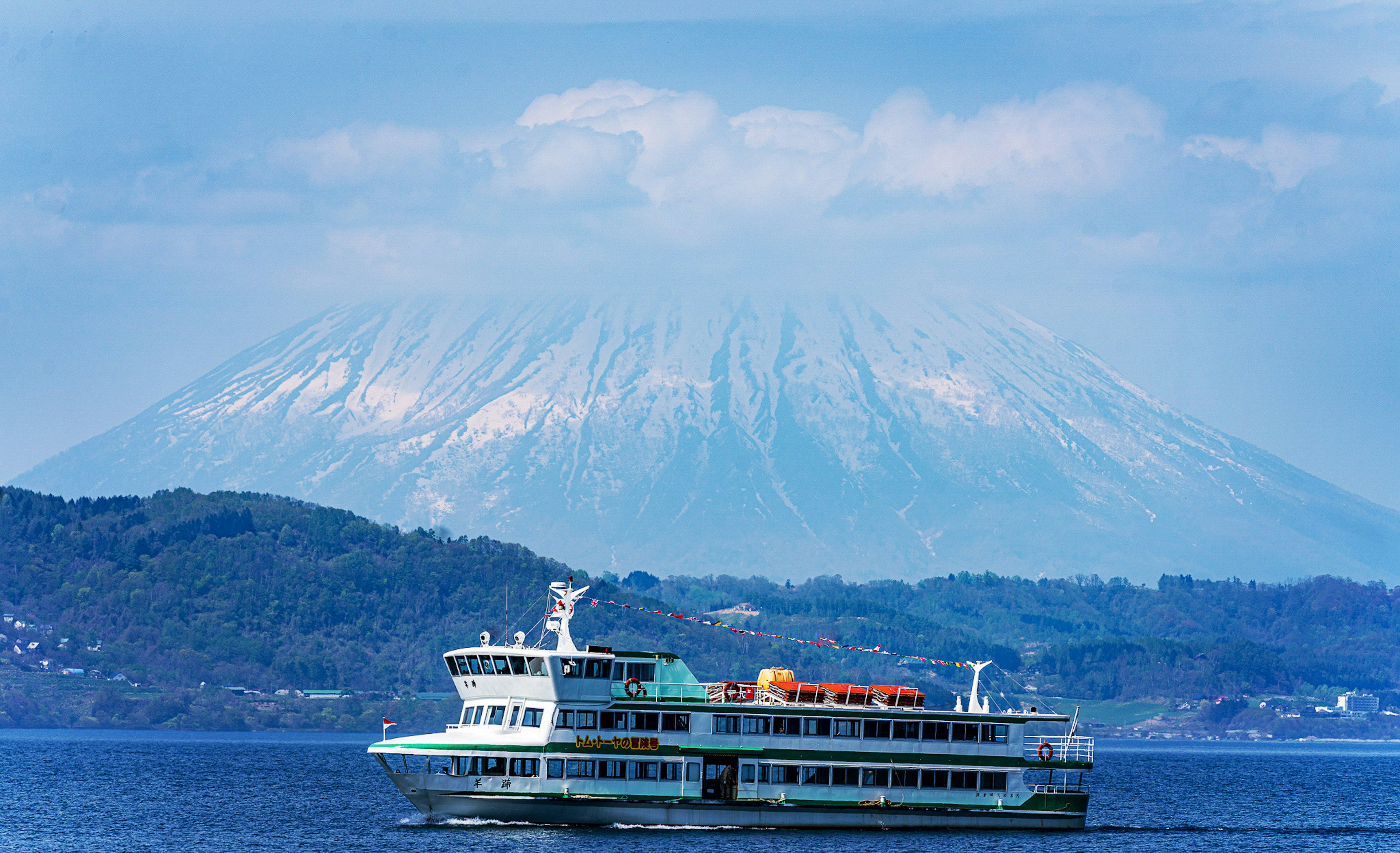 Ferry sailing on blue waters with a snow-capped mountain in the background