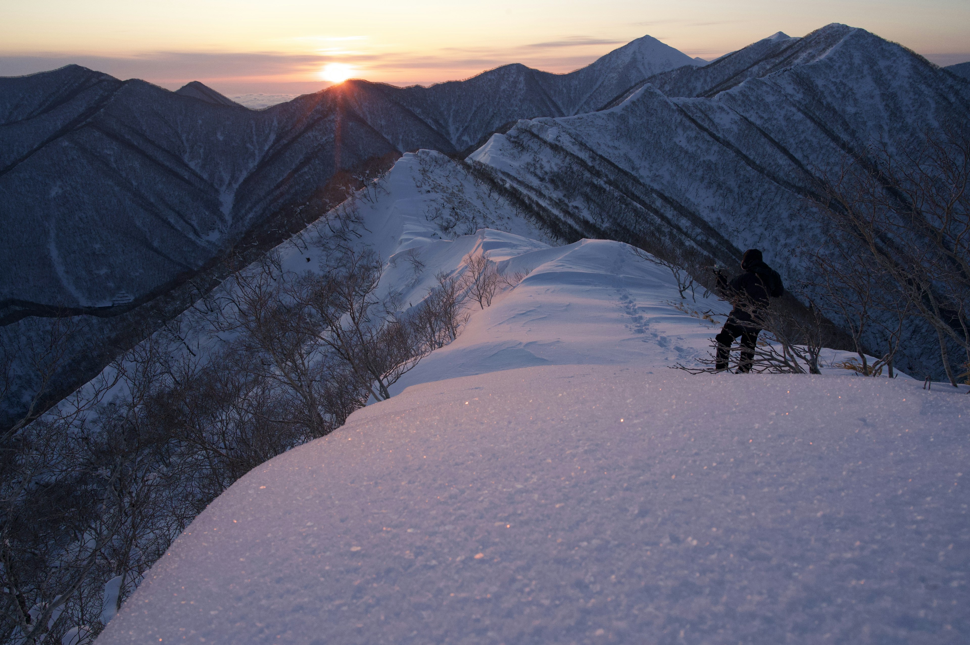 雪に覆われた山脈と夕日を背にした登山者