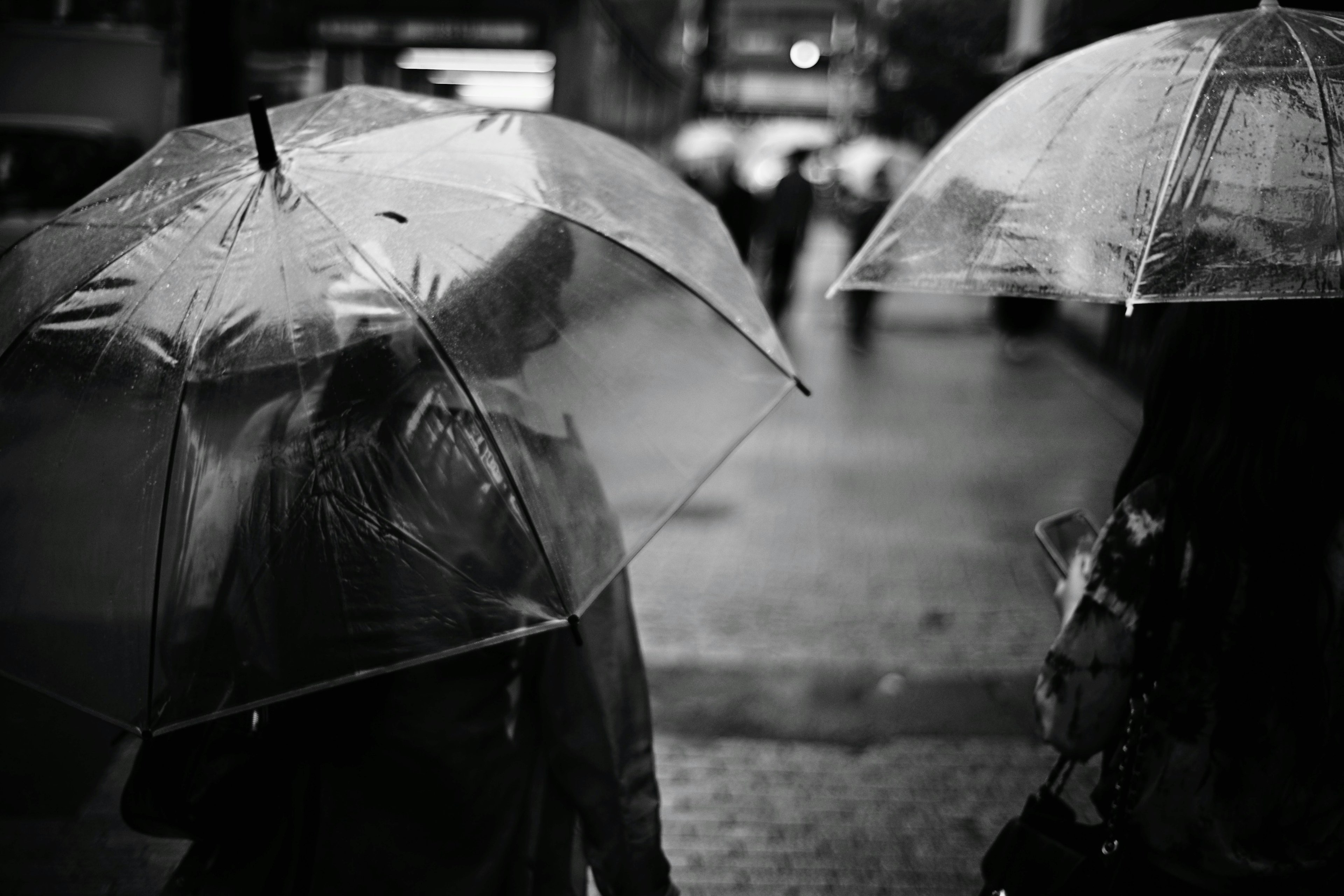 雨の中で透明な傘を持つ二人の人が歩いているモノクロ写真