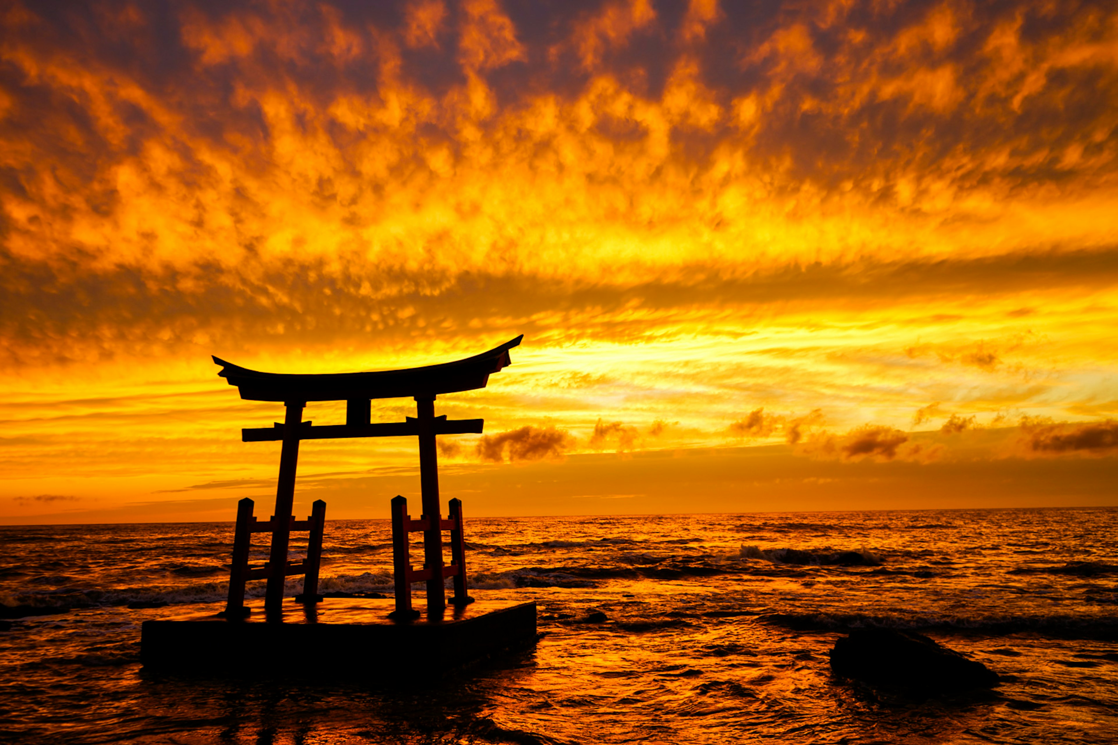 Torii im Silhouetten gegen einen lebhaften Sonnenuntergang über dem Ozean